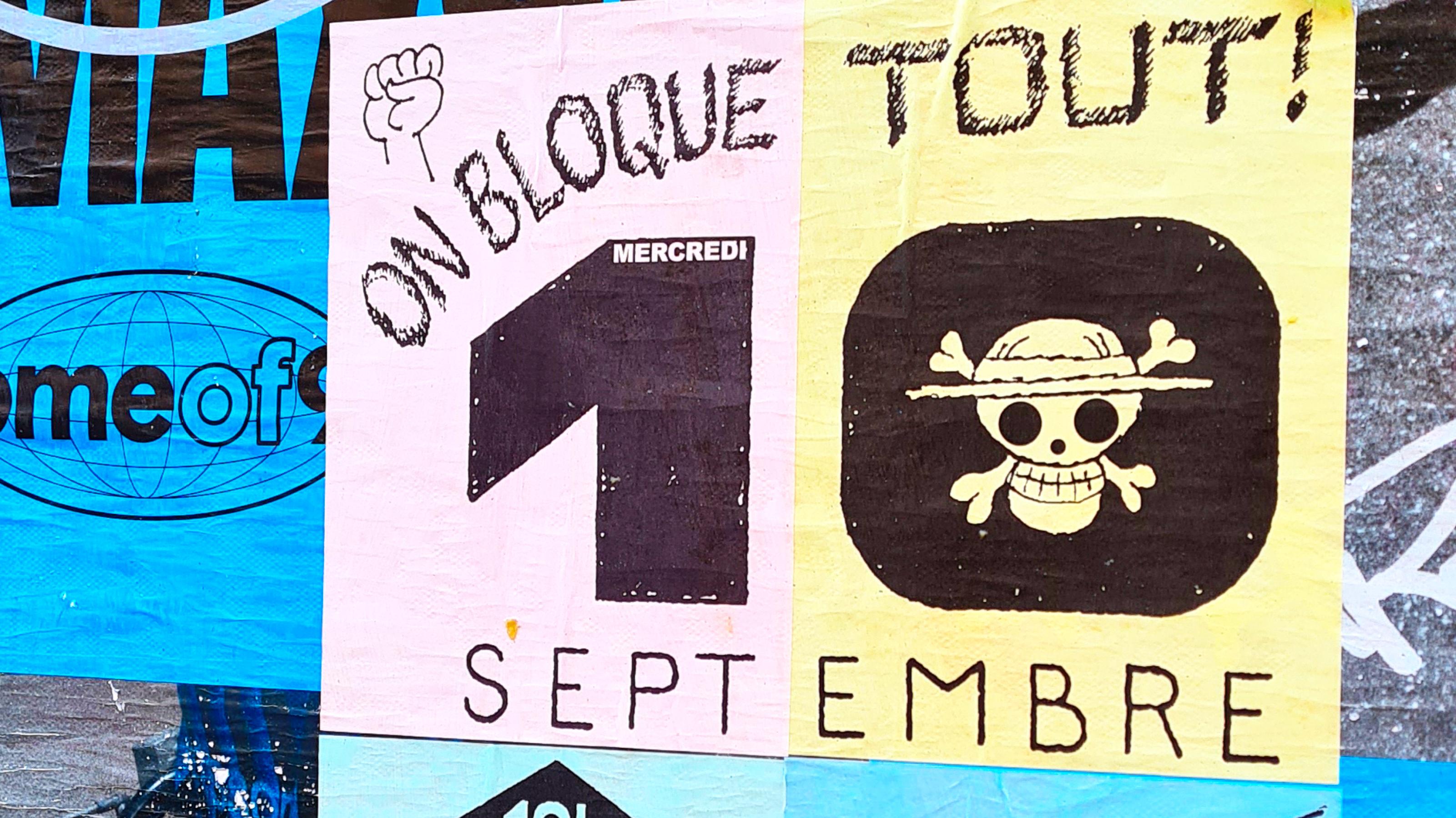Plakat mit einem Riss in der unteren linken Ecke. Oben auf dem Plakat liest man „Wir blockieren alles“ auf Französisch, gefolgt vom „10. September“. Im Null ist ein mit einem Hut bekleideter Totenkopf zu sehen. Unten rechts gibt es drei Pfeile mit jeweils einem Satz: „Wir gehen nicht zur Arbeit“, „Wir demonstrieren zusammen“, „Ihre Austerität, nein!“.