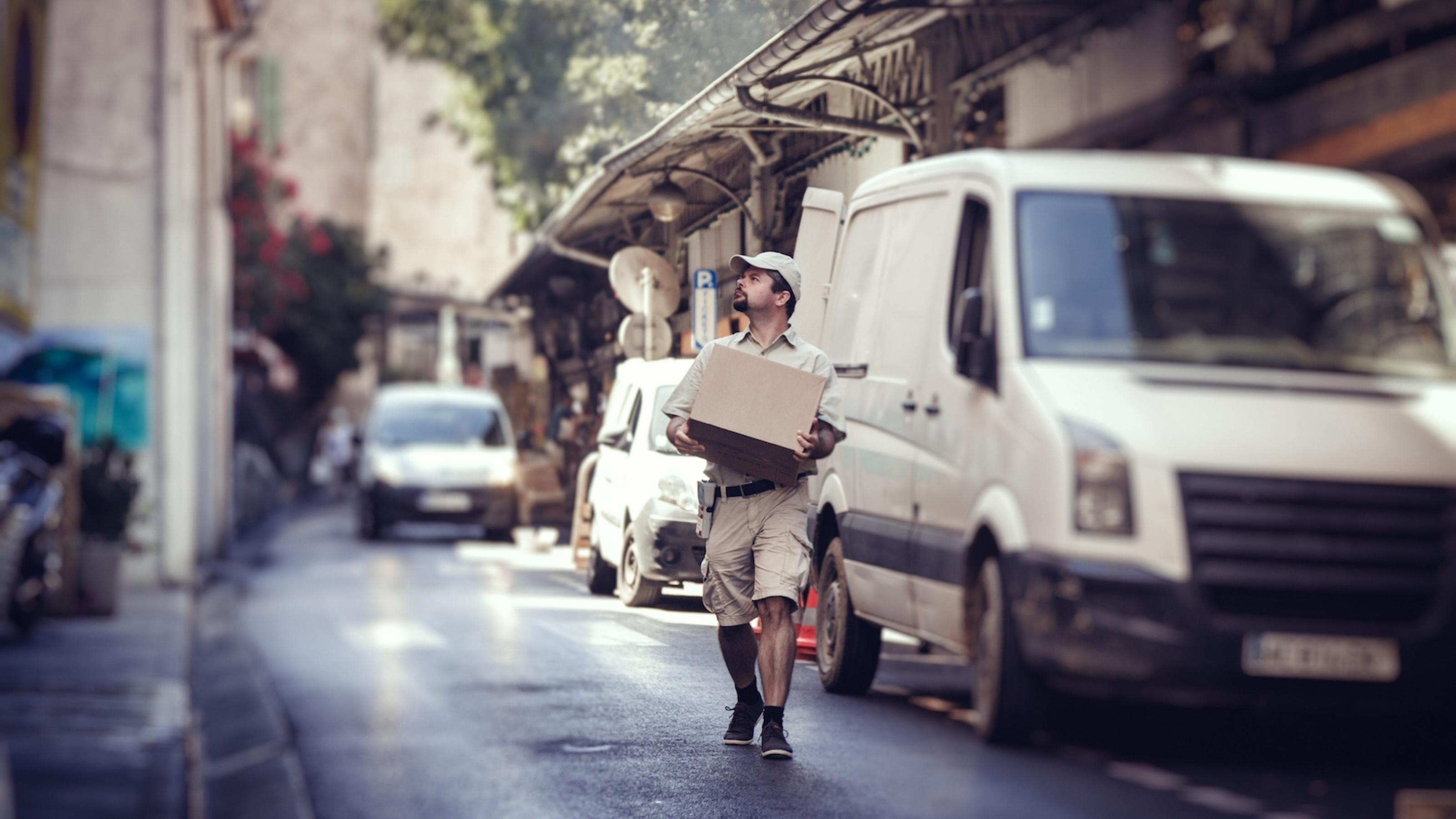 Ein Paketzusteller hält ein Paket in der Hand und läuft über die Straße