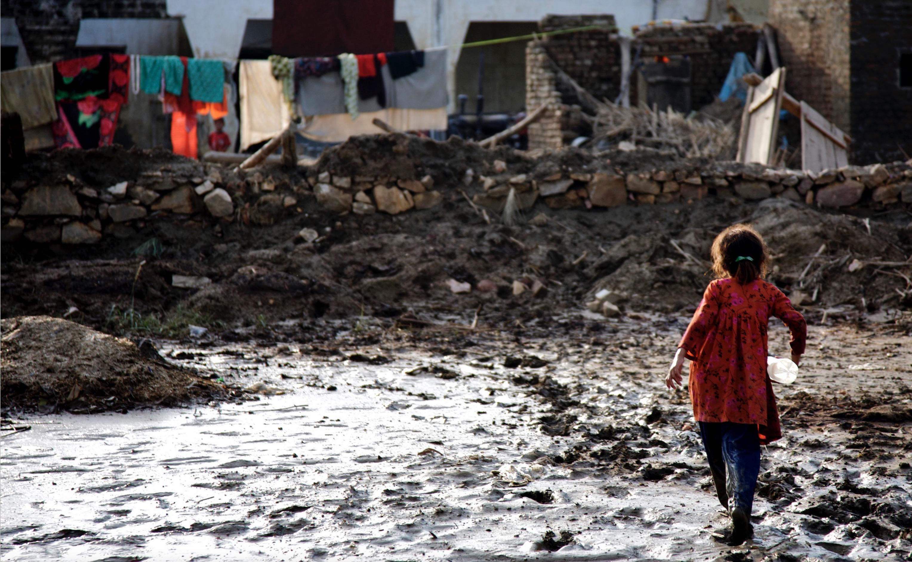 Ein Mädchen mit einer Plastik-Wasserflasche unter dem Arm läuft an einer matschigen Pfütze entlang, die von einer zurückgehenden Überschwemmung zurückgeblieben ist.