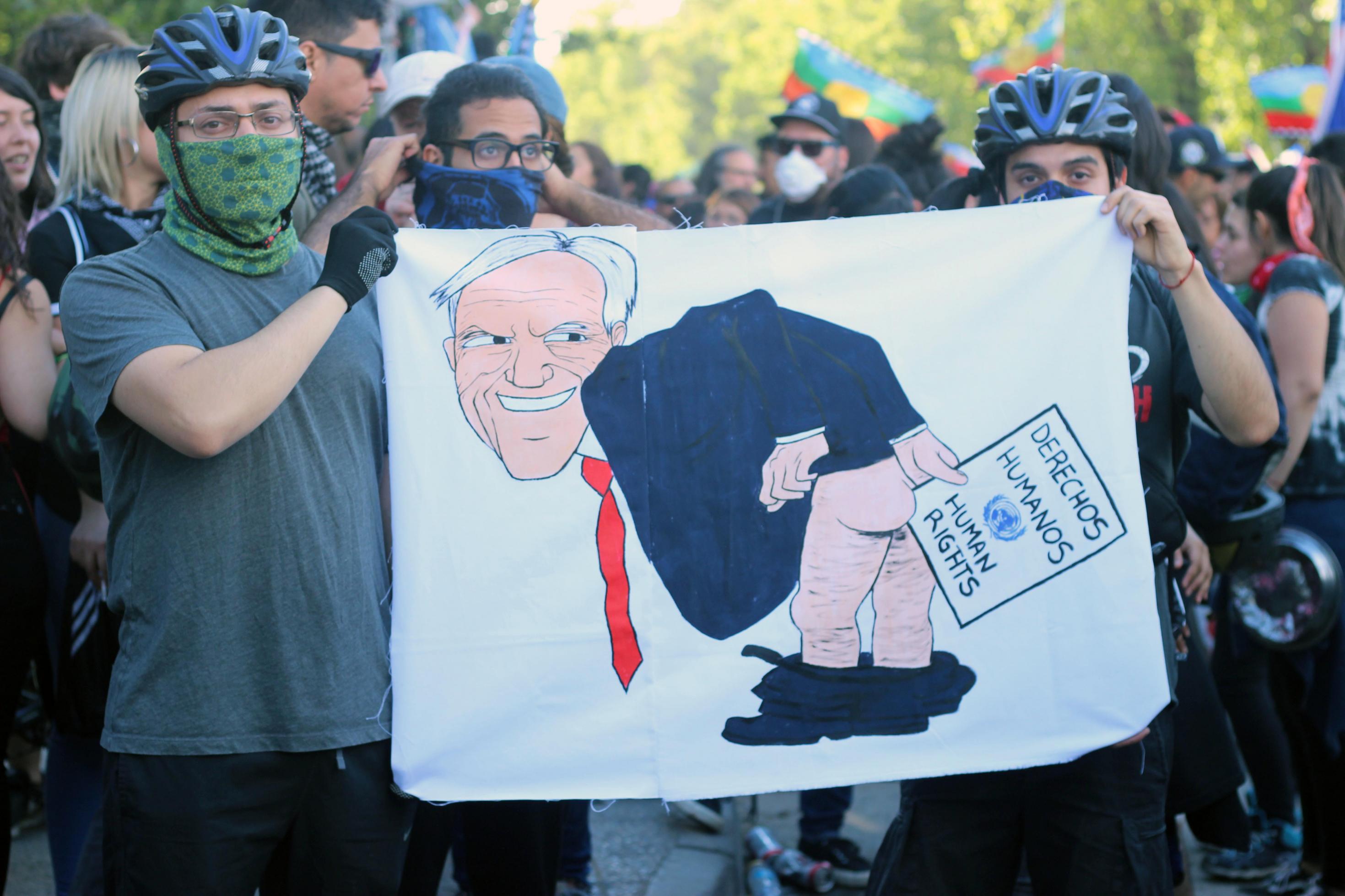 Demonstrantinnen halten ein Schild hoch mit einem Bild von Präsident Piñera, die Menschenrechtserklärung als Klopapier benutzt.