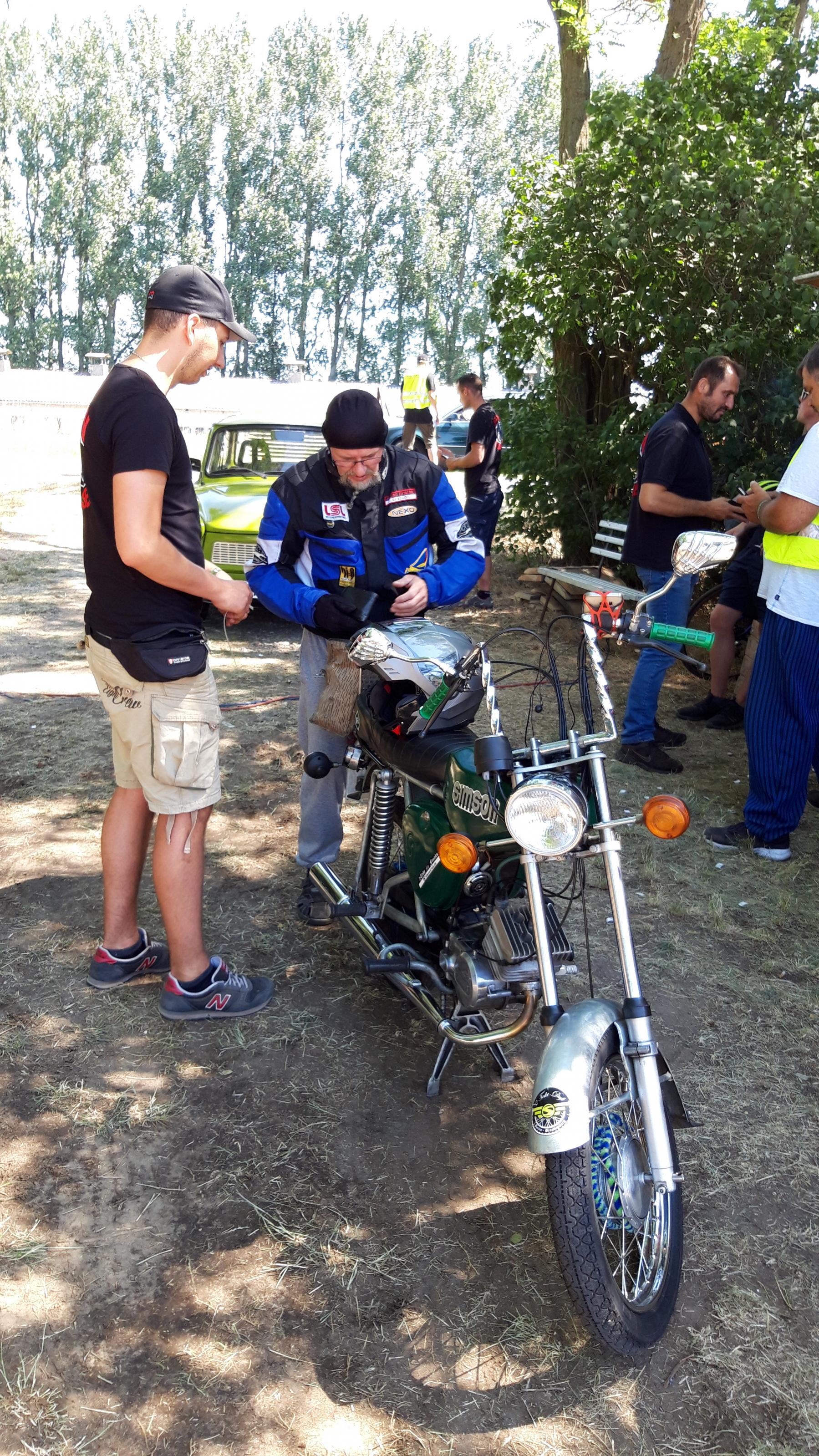 Ein Baseballbemützter kassiert von einem Motorradfahrer das Eintrittsgeld.