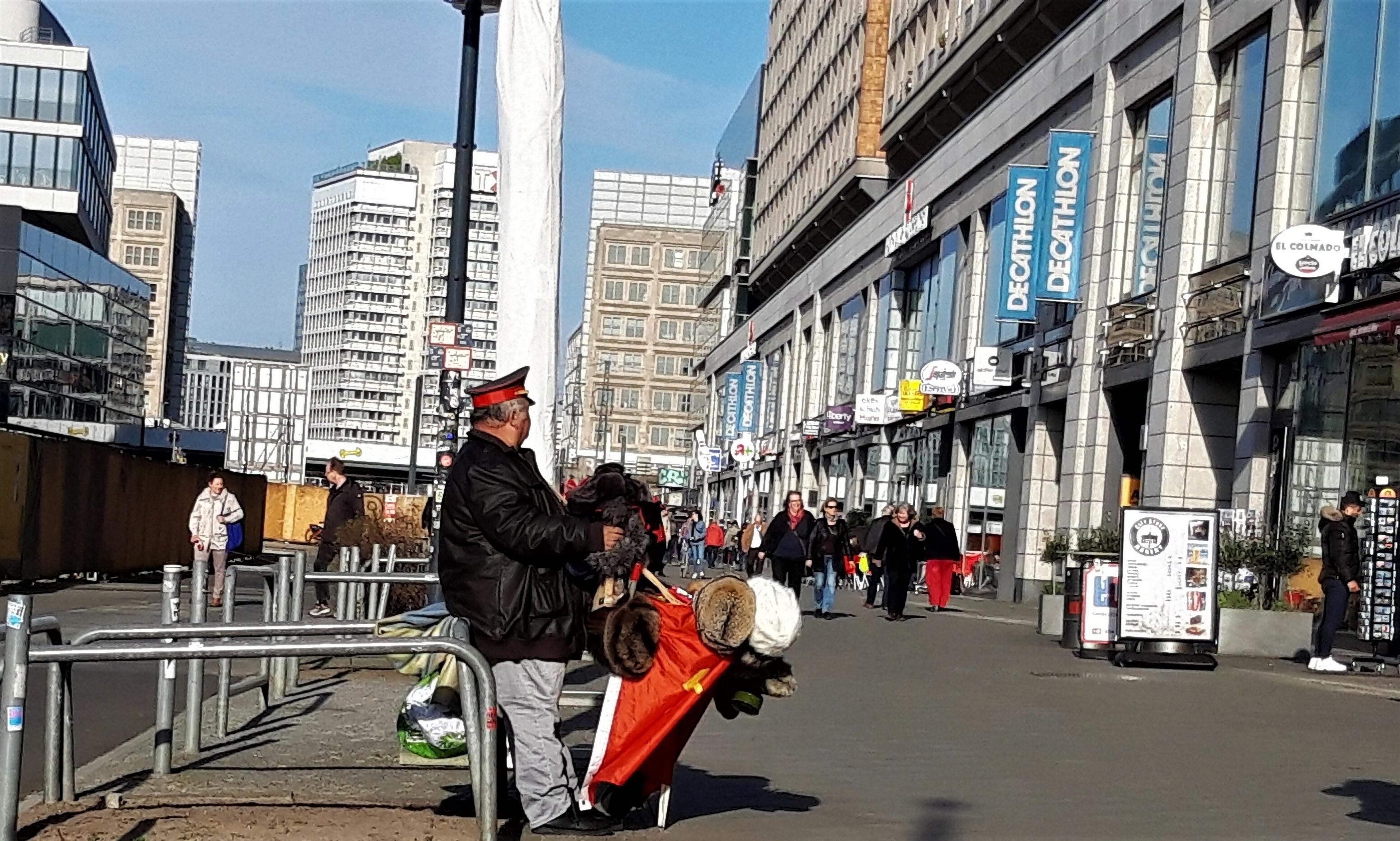 Ein untersetzter Mann hat eine Sowjet-Uniformmütze auf und verkauft Pelzmützen und andere Sowjet-Souvenirs