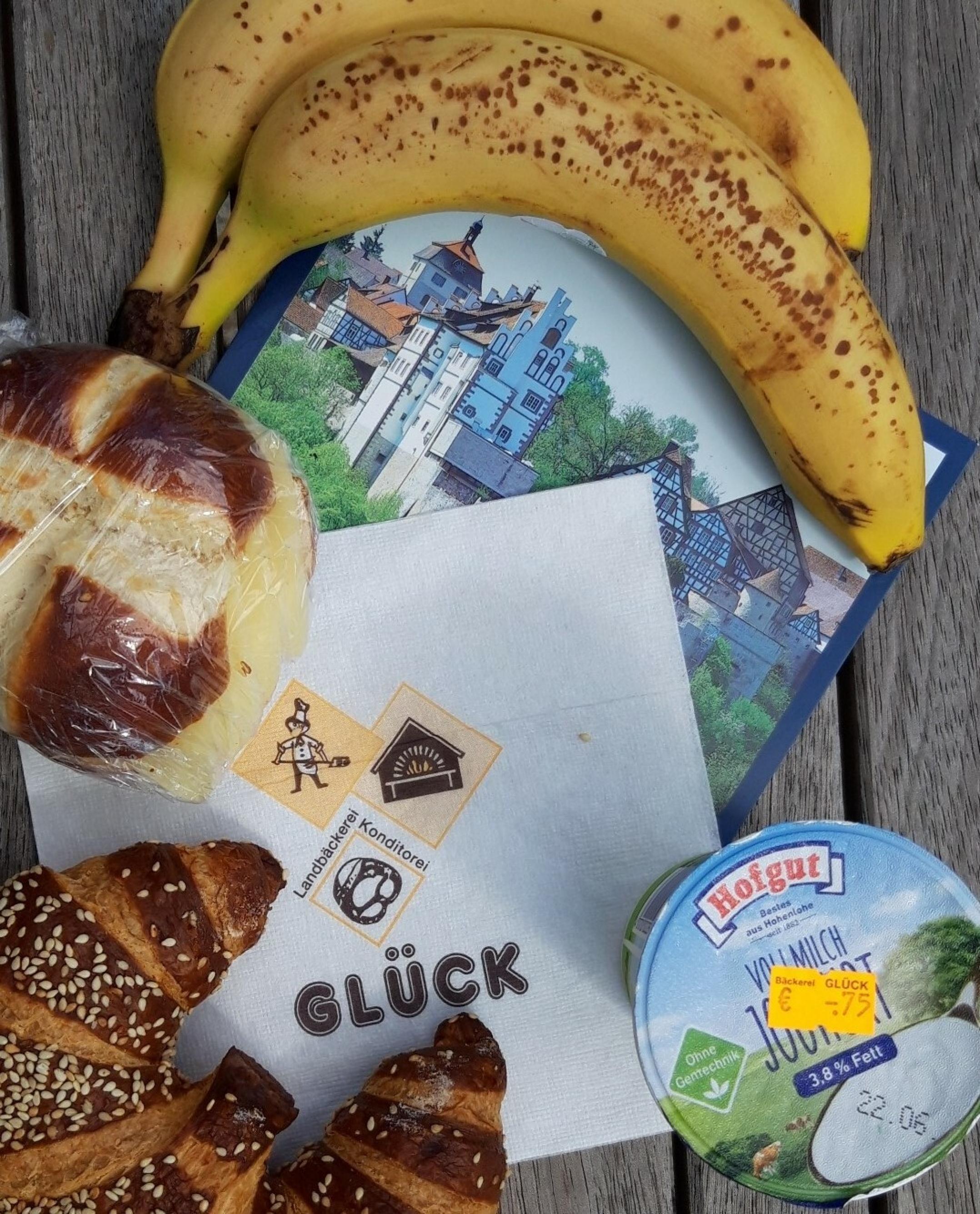 Stillleben auf einer Parkbank mit Banane, Joghurt, Laugenbrötchen.