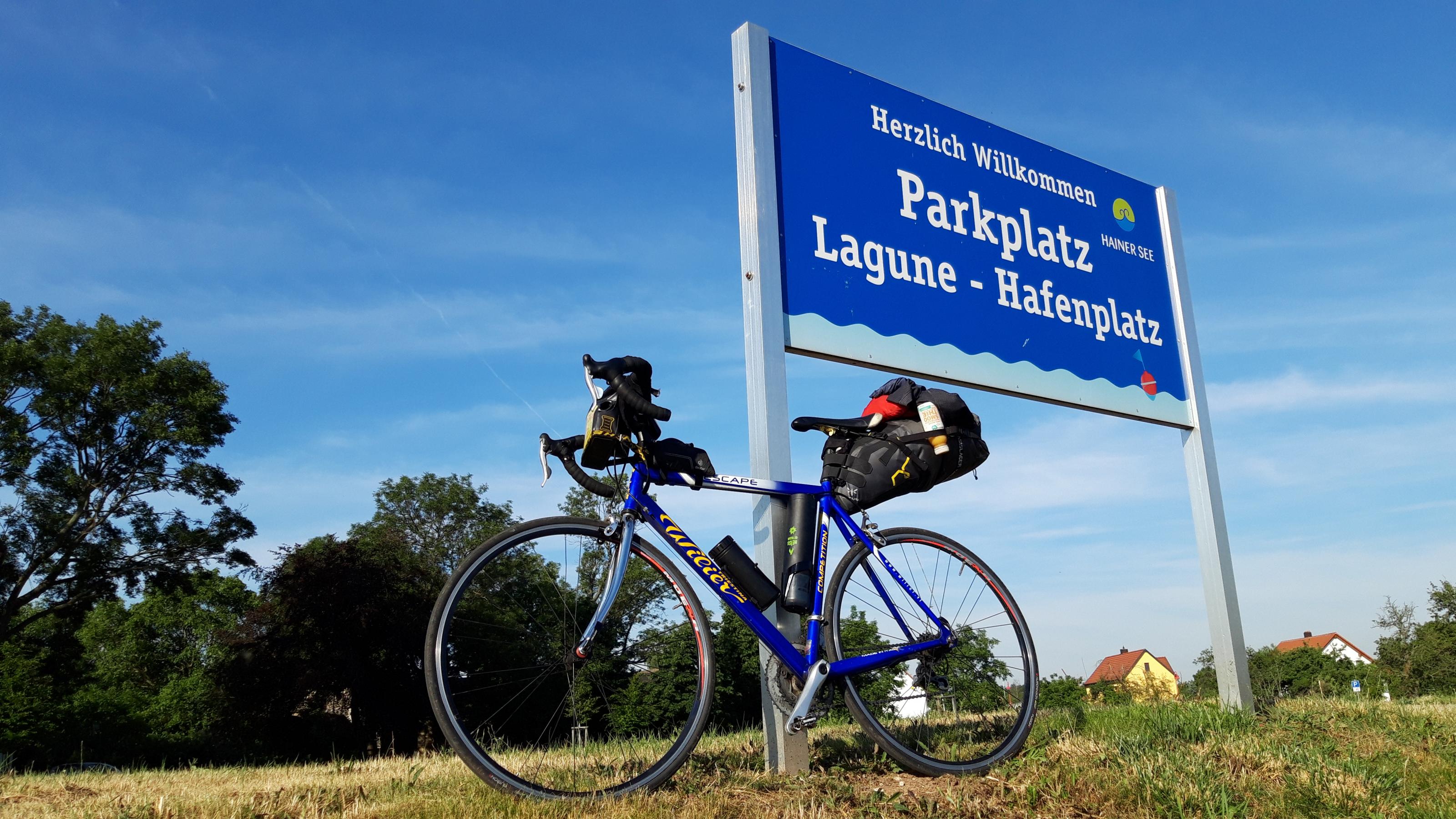 Das Rad lehnt an einem Schild mit der Aufrschrift Parkplatz Lagune – Hafenplatz Hainer See.