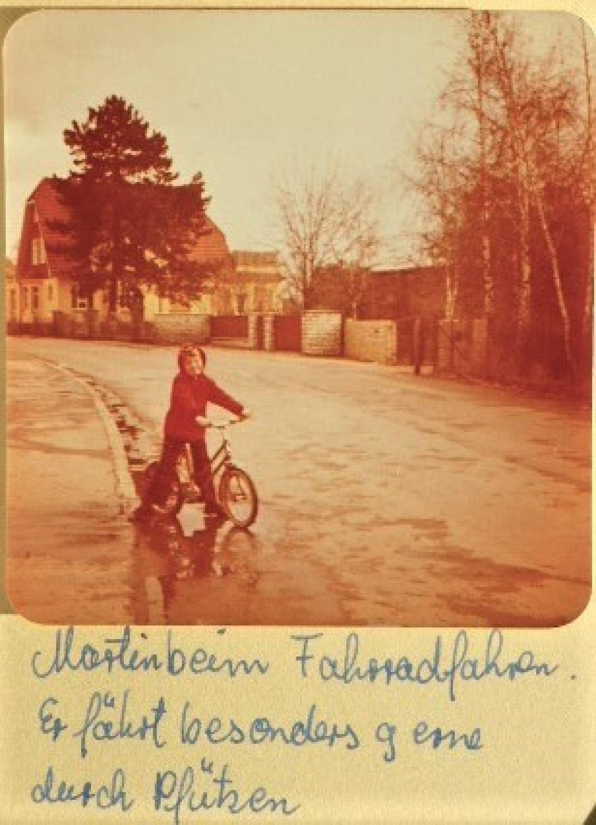 Kleinkind Martin C Roos auf seinem Erstrad, Aufnahme im Familienalbum handschriftlich ergänzt durch den Satz „Er fährt besonders gern durch Pfützen“.