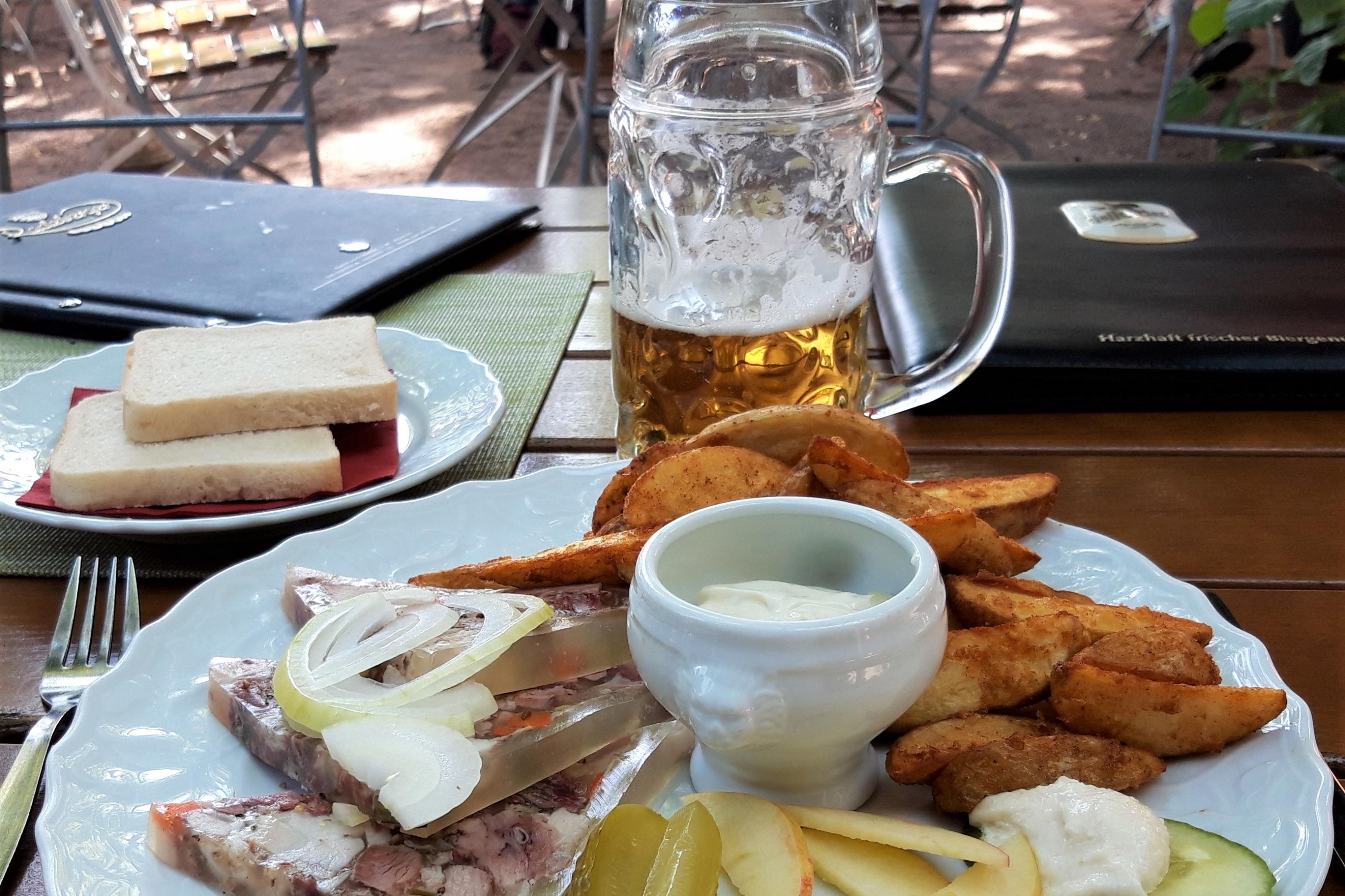 Ein Teller mit Kartoffeln, Sülze, Tellergarnitur und einem halb getrunkenen Bierglas.