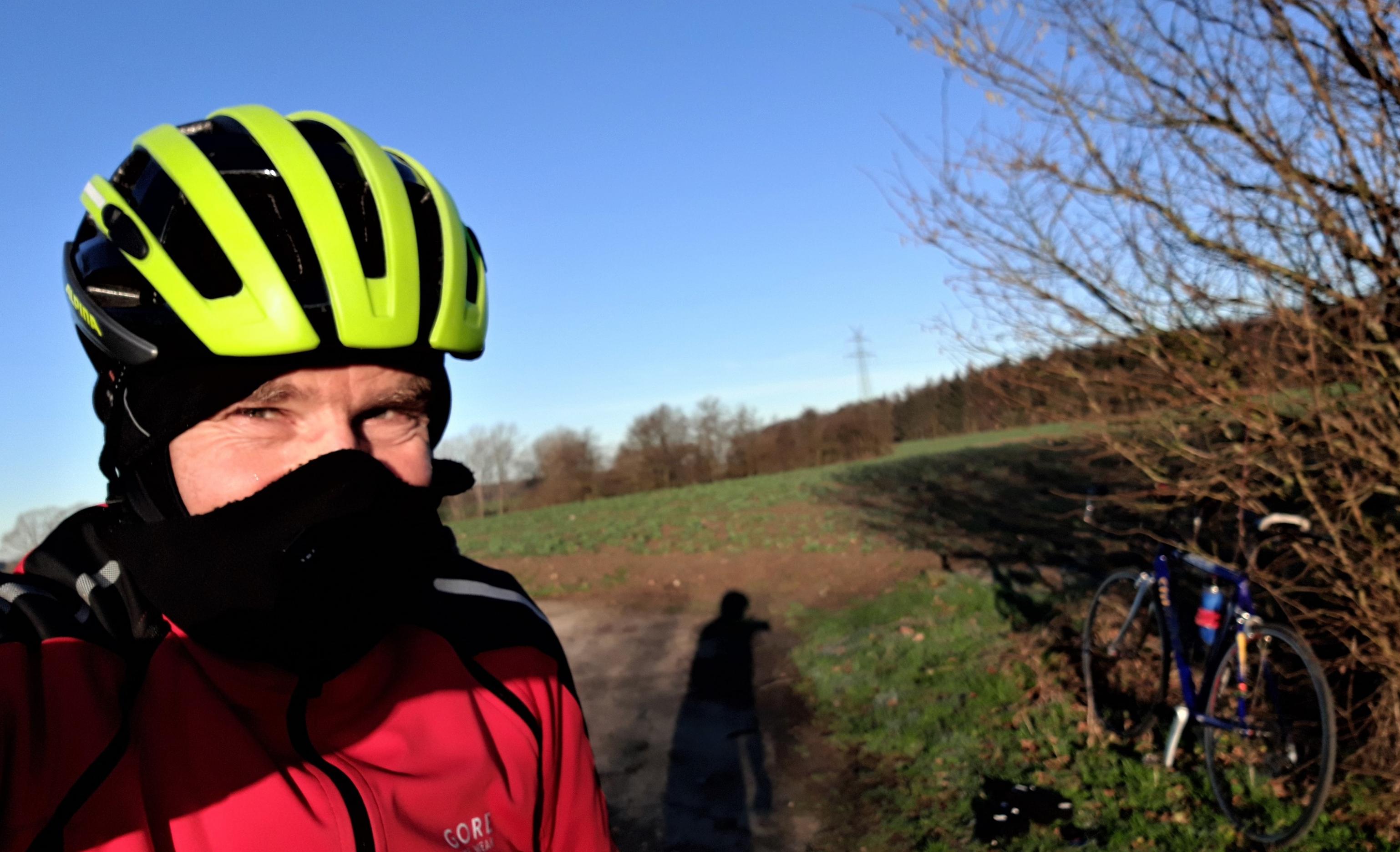 Radfahrer mit Helm, Sturmhaube und Nasenschutz vor Winterlandschaft.