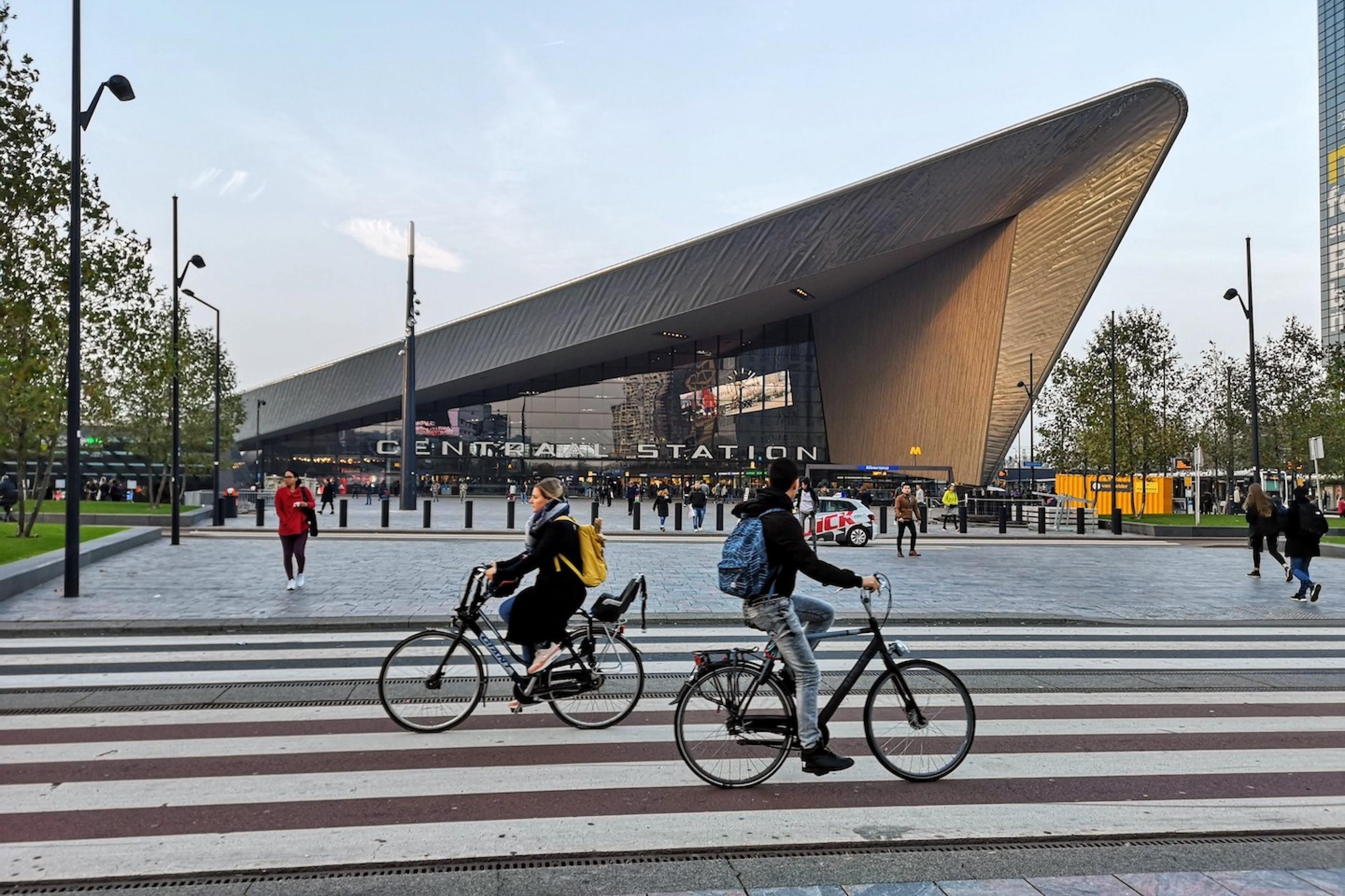 Der Bahnhof in Rotterdam. Im Vordergrund fahren zwei Radfahrer aneinander vorbei.