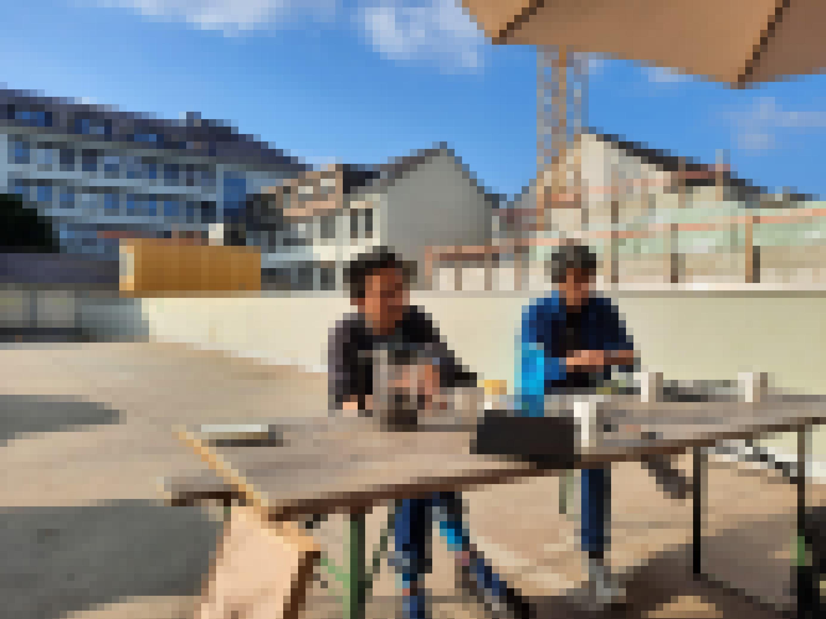 Reza Afisina und Iswanto Hartono sitzen bei schönem Wetter an einem Biertisch auf dem Parkdeck des ruruHauses in Kassel.