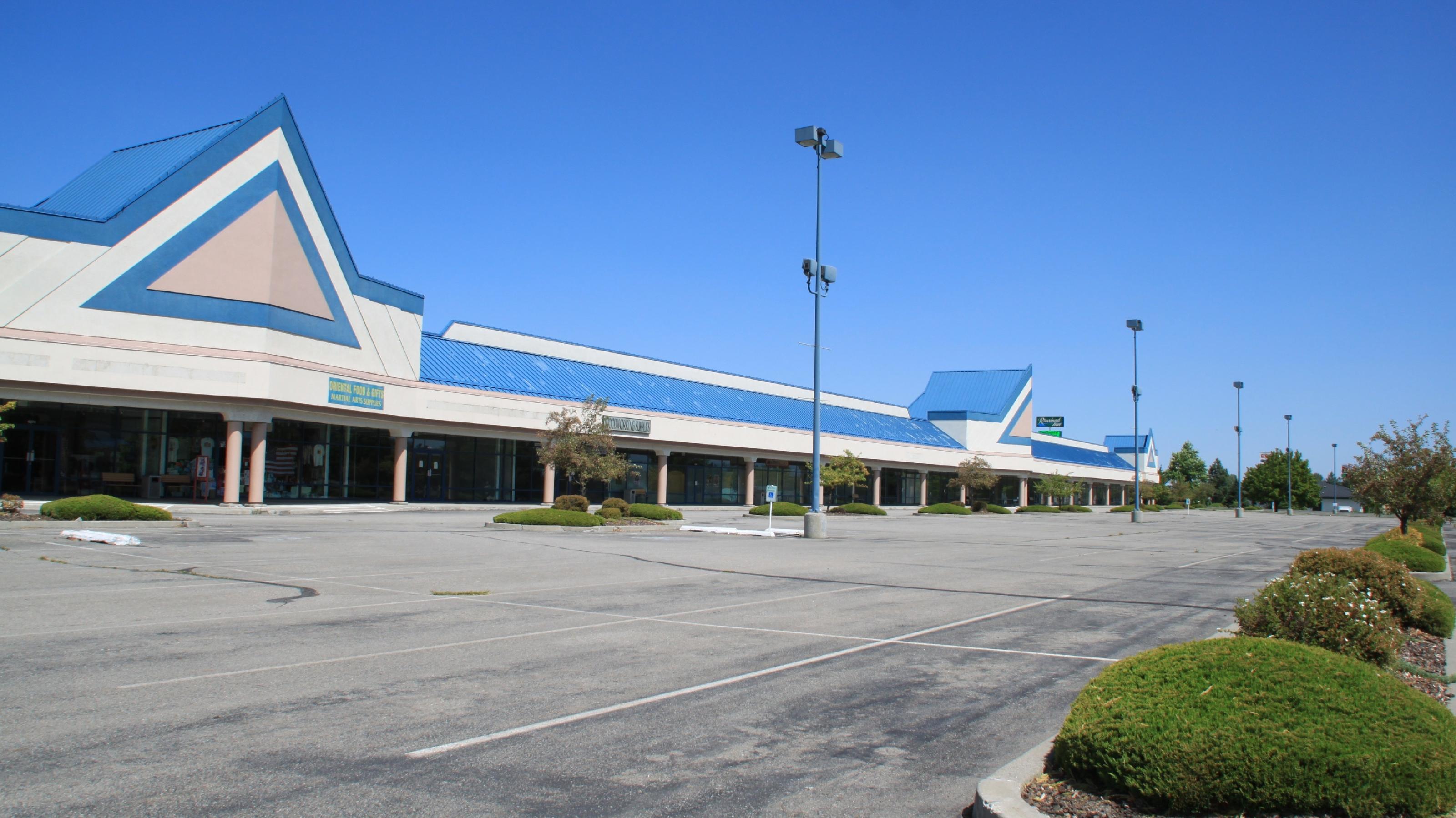 Ein Einkaufszentrum mit einem leeren Parkplatz vor blauem Himmel.