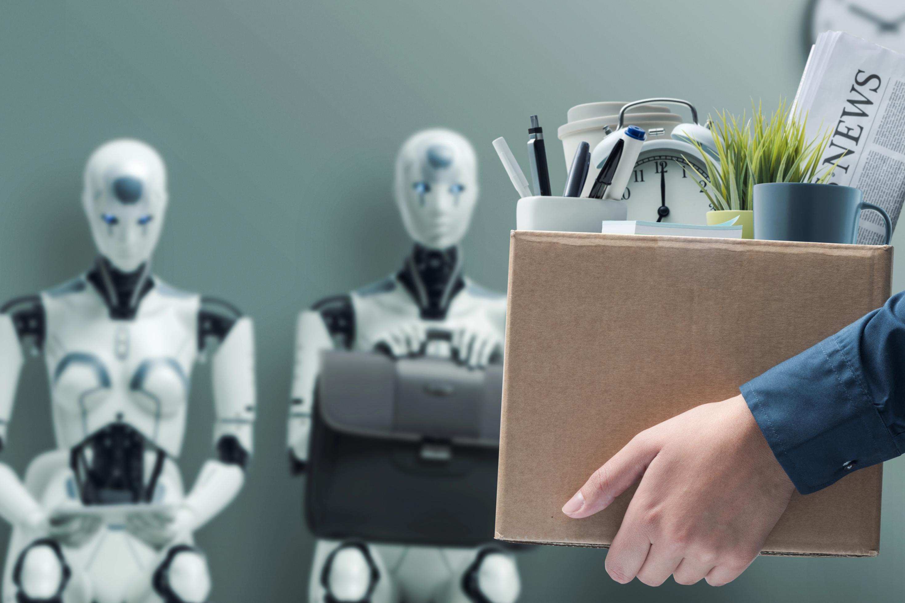 Ein Mitarbeiter verlässt das Büro mit seinen persönlichen Sachen. Im Hintergrund warten schon Roboter auf ein Jobinterview. Symbolbild für Arbeitslosigkeit durch KI.