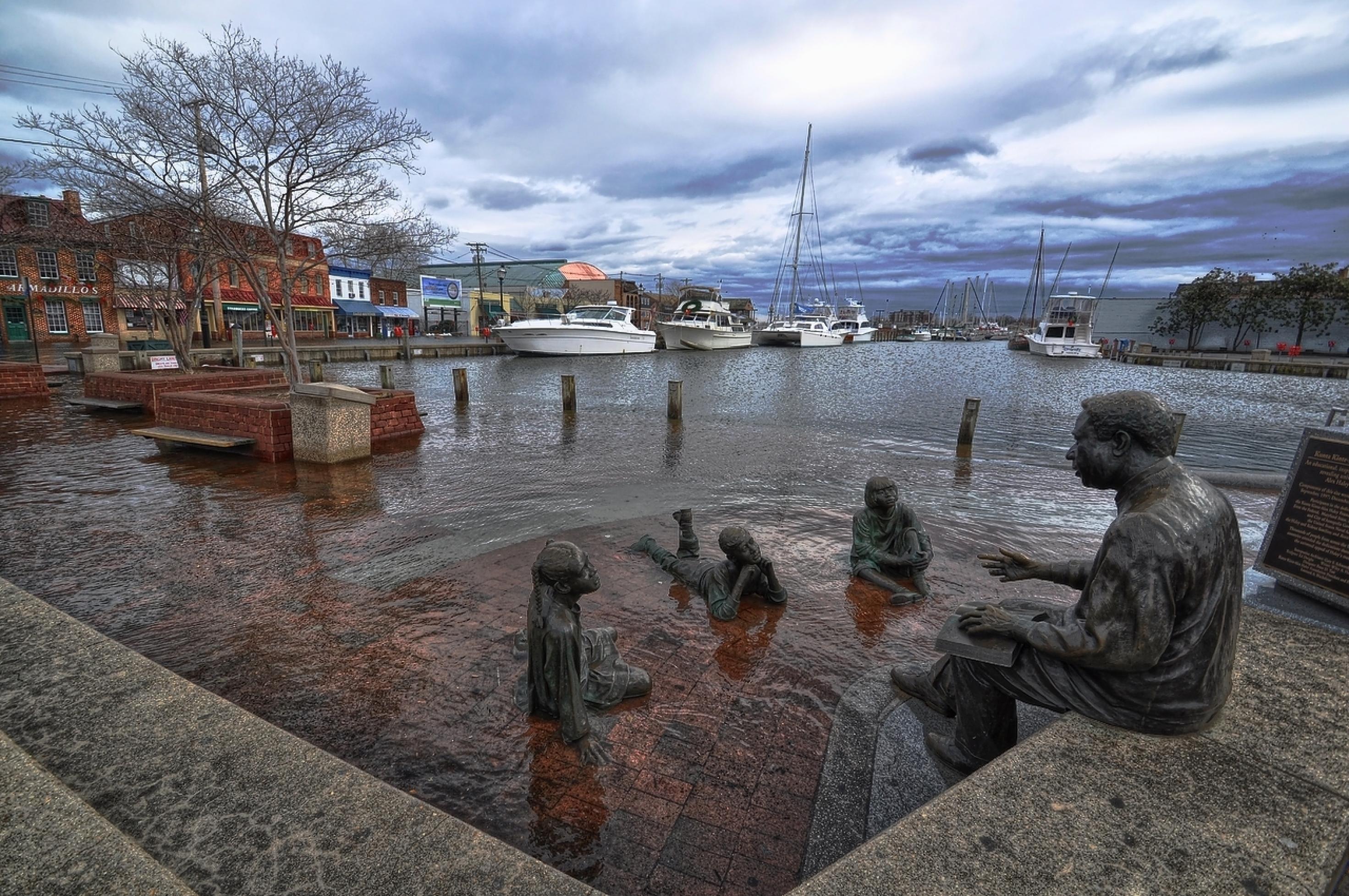 Vier Bronzefiguren: Ein alter Mann liest eine Geschichte aus einem Buch vor, drei Kinder liegen vor ihm auf dem Boden und hören zu. Doch die Skulptur im Hafen von Annapolis/Maryland, die den Schriftsteller Alex Halley und seine „Roots“-Saga ehrt, wird immer wieder überflutet. Hier umspült das Wasser die Figuren der Kinder. Manchmal guckt nur noch der Kopf des Alten aus dem Wasser.