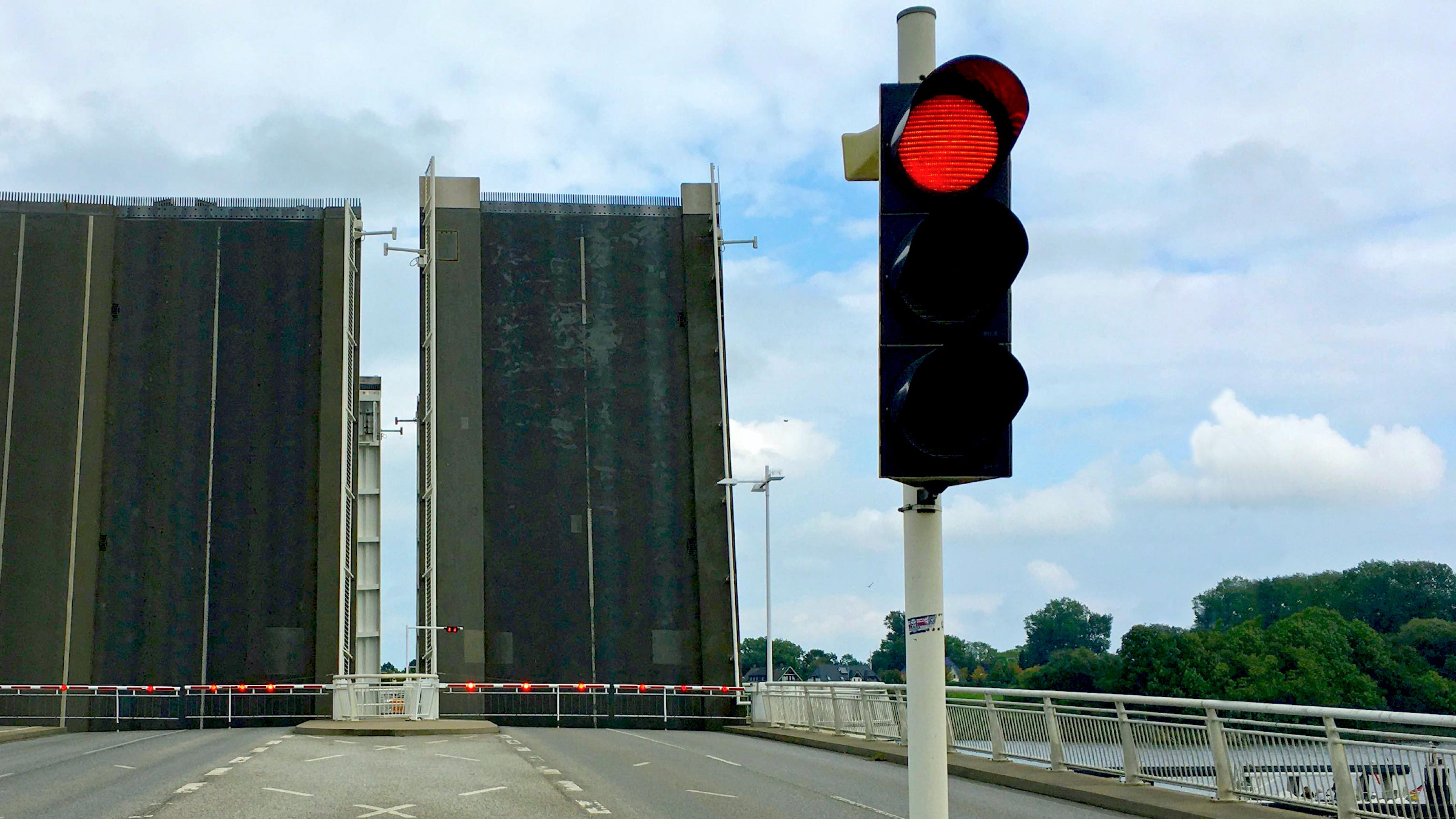 Eine Klappbrücke, hier in Kapseln an der Schlei, ist hochgeklappt, davor sperrt eine rote Ampel die Straße für den Verkehr.
