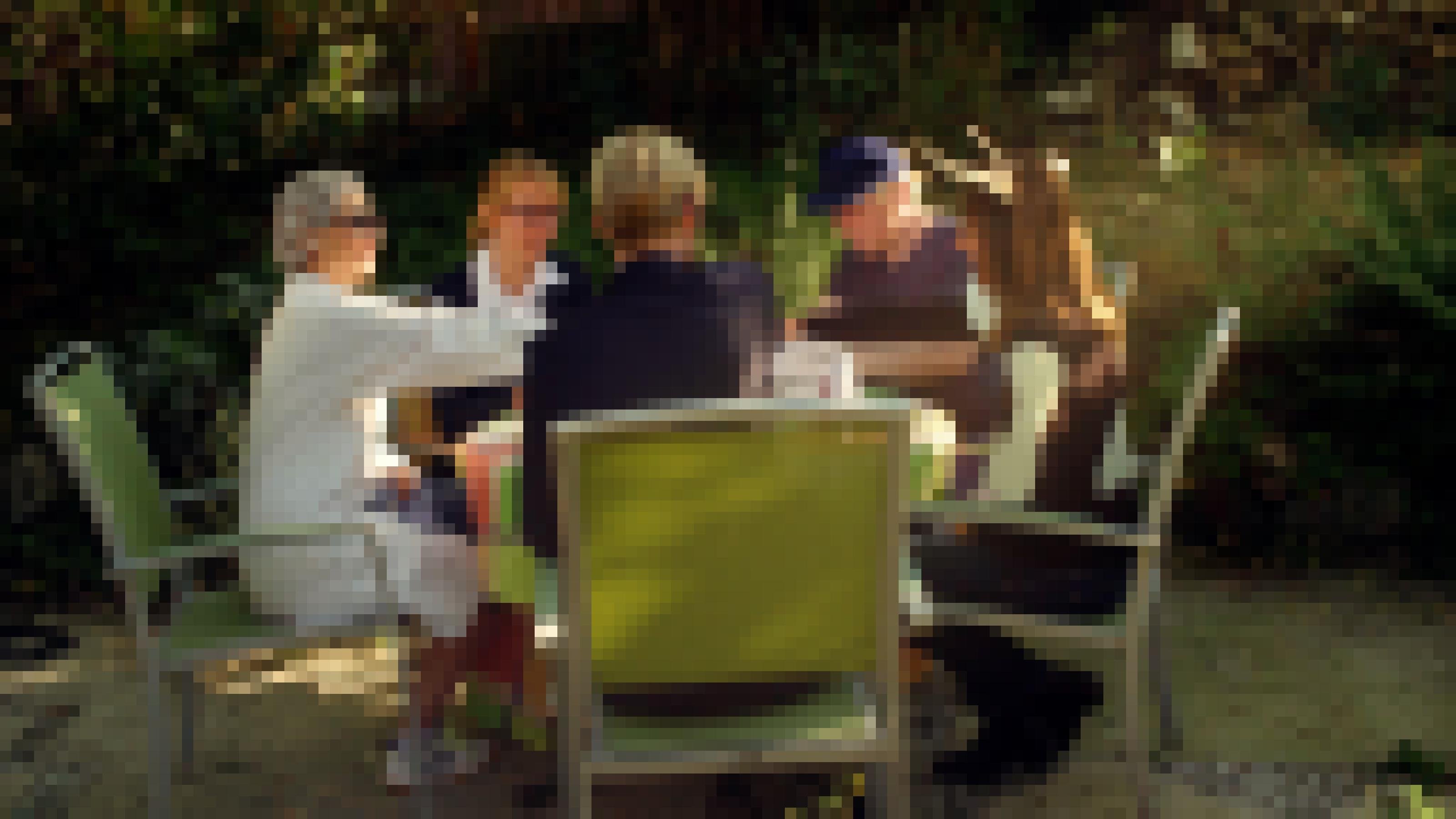 In einem Garten sitzen fünf Menschen an einem Tisch.