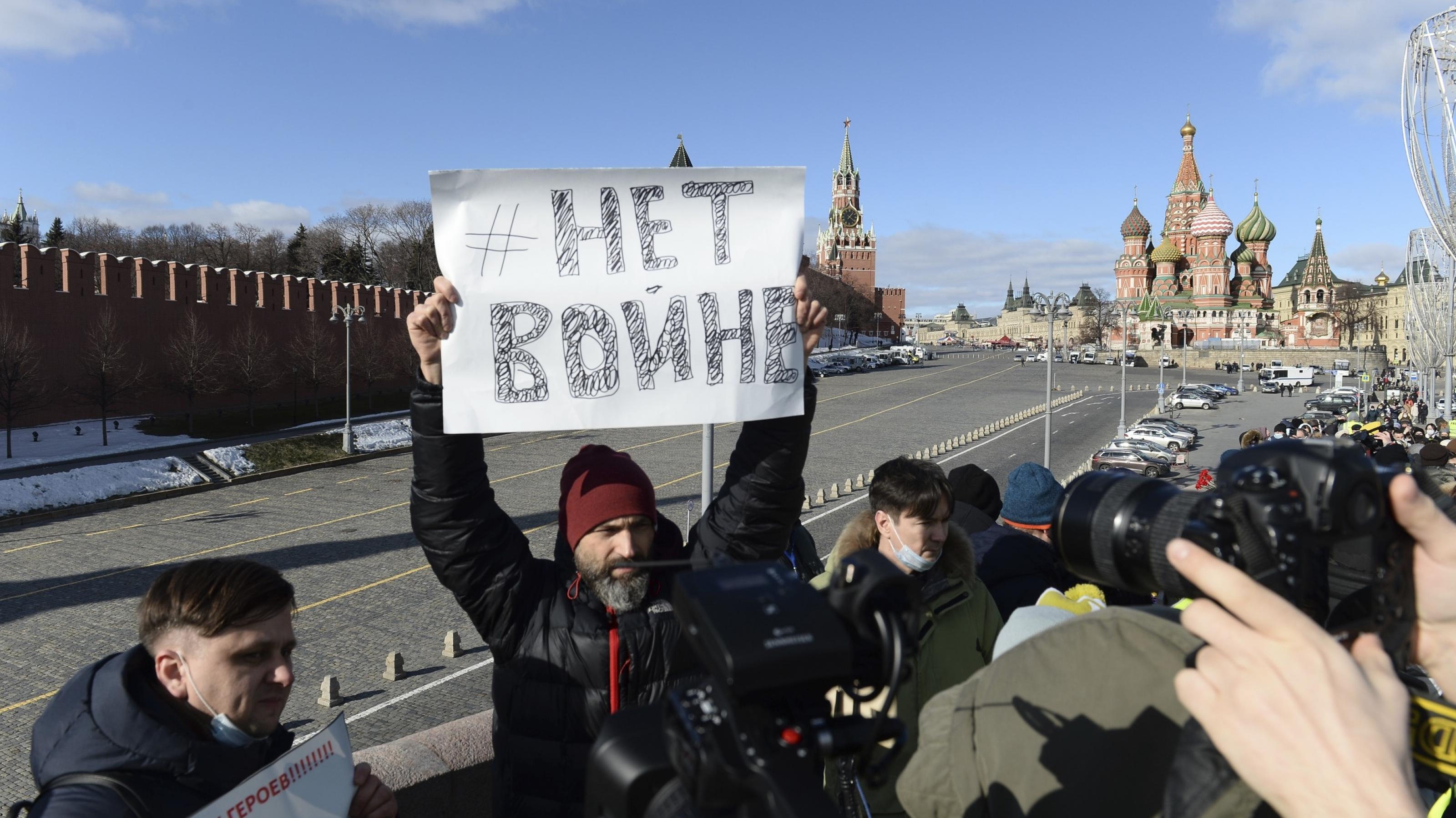 Mann hält ein Schild mit der Aufschrift  „Kein Krieg“ hoch. Im Hintergrund ist die Basilius-Kathedrale des Kreml zu sehen.