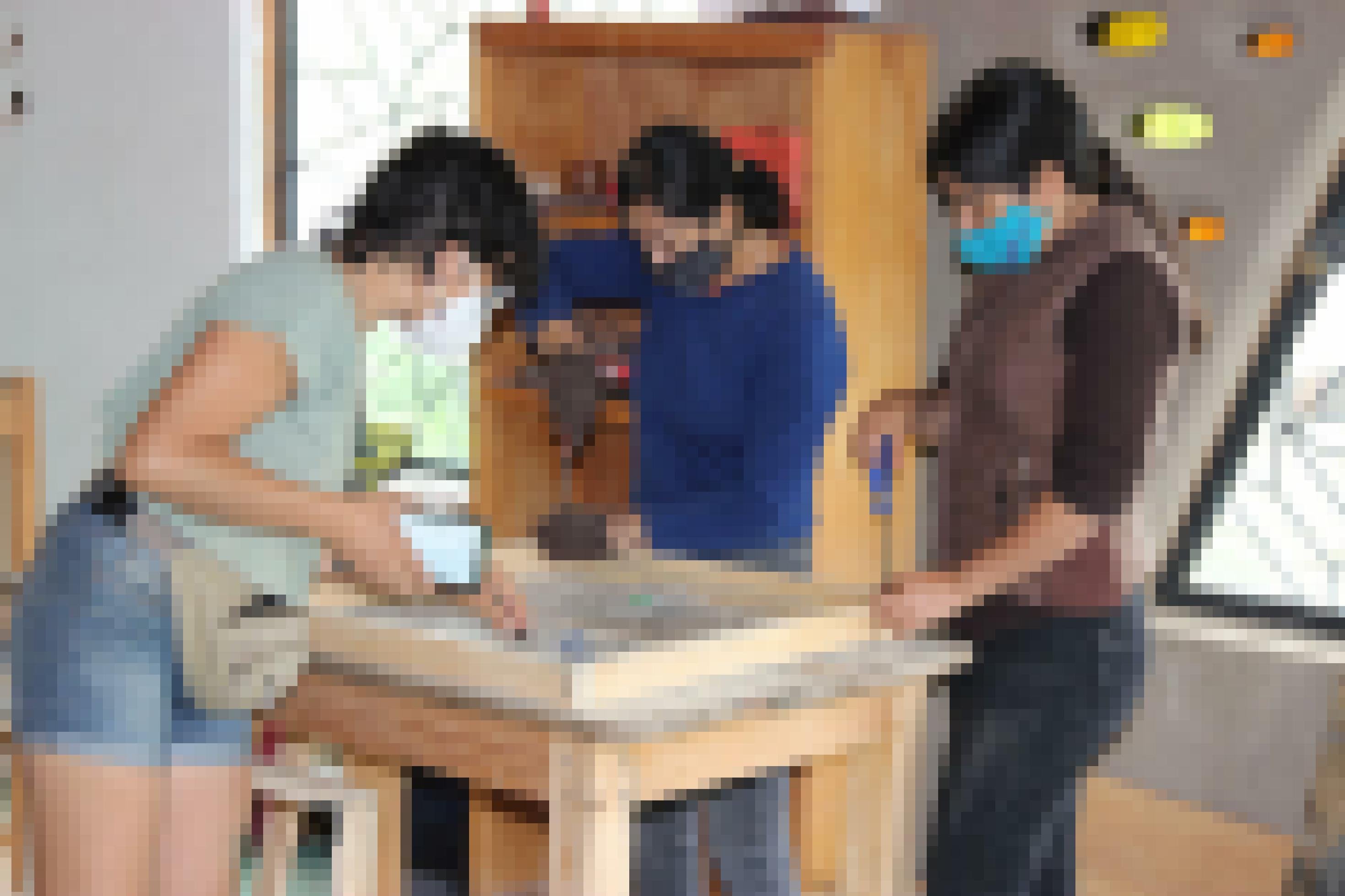 eine Gruppe von Frauen, die Gesichtsmasken tragen, arbeitet an einem Holztisch [AI]