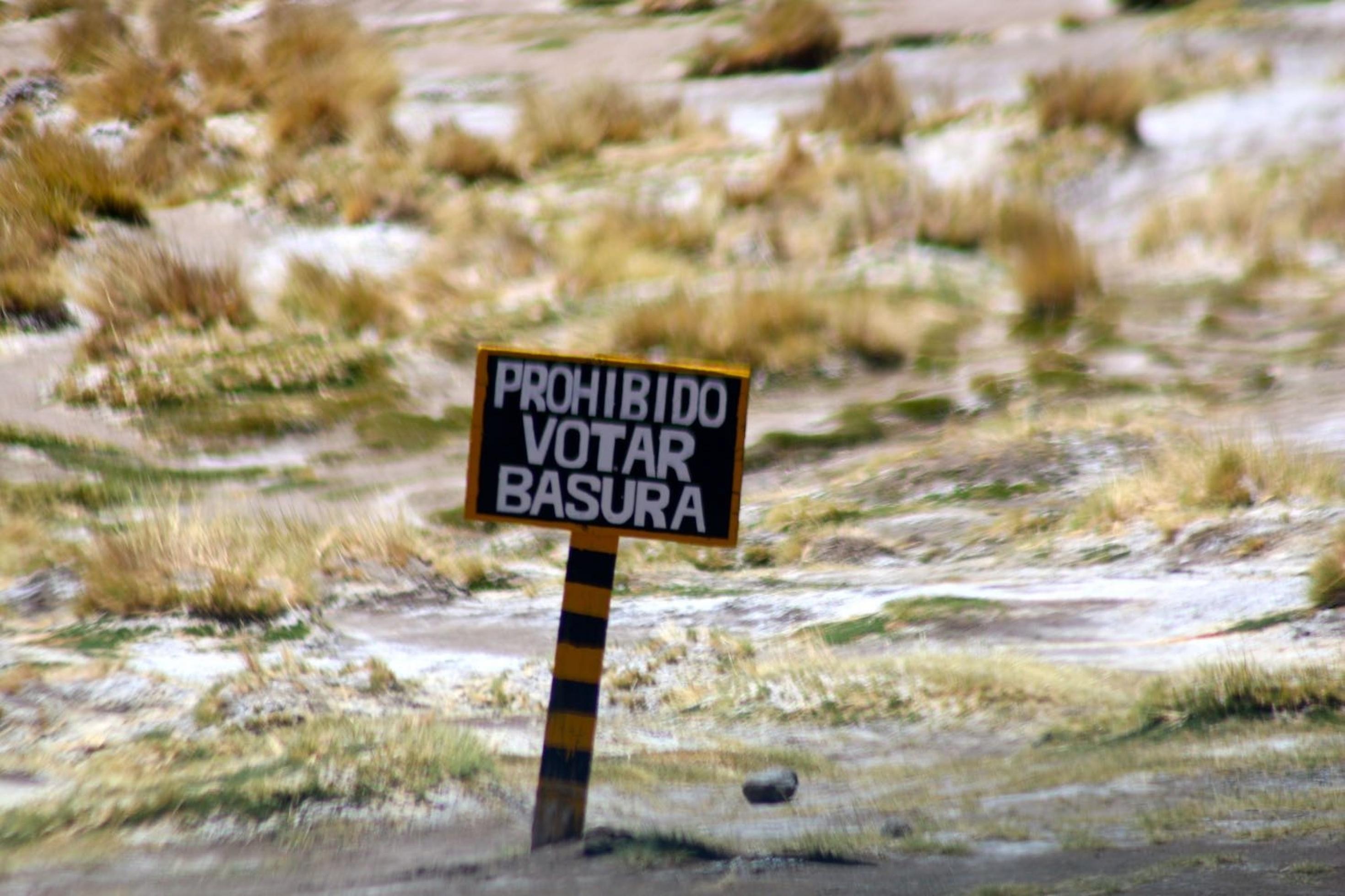 Ein Holzschild steht leicht nach rechts geneigt in einer steppe-ähnlichen Landschaft, wo Grasbüschel aus dem Sand ragen. Darauf steht: „Prohibido votar basura“. –
„Müll abladen verboten“ – das sollte wohl auf diesem Schild in der bolivianischen Hochebene stehen. Durch einen Schreibfehler ist eine politische Weisheit daraus geworden: „Müll wählen verboten“.