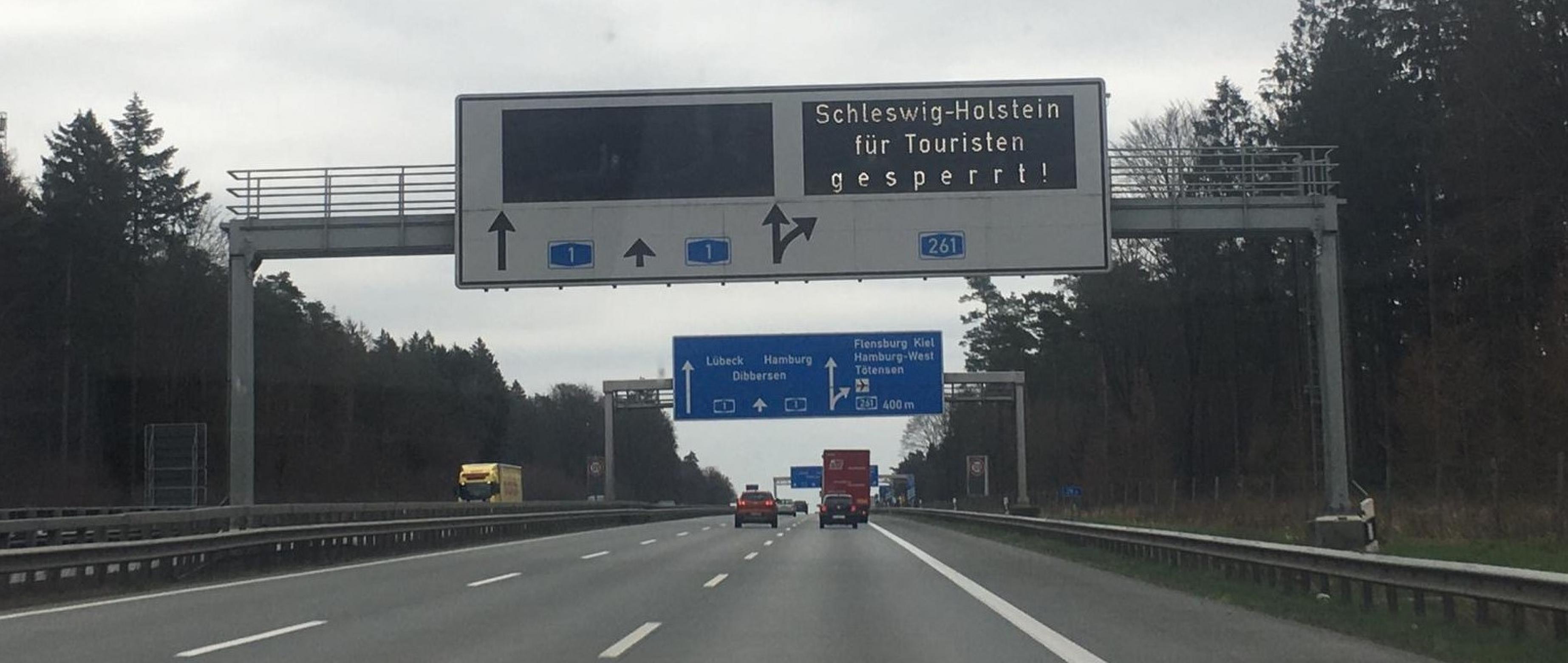 Ein Schild über der Autobahn zeigt folgende Aufschrift: „Schleswig-Holstein ist für Touristen gesperrt“.