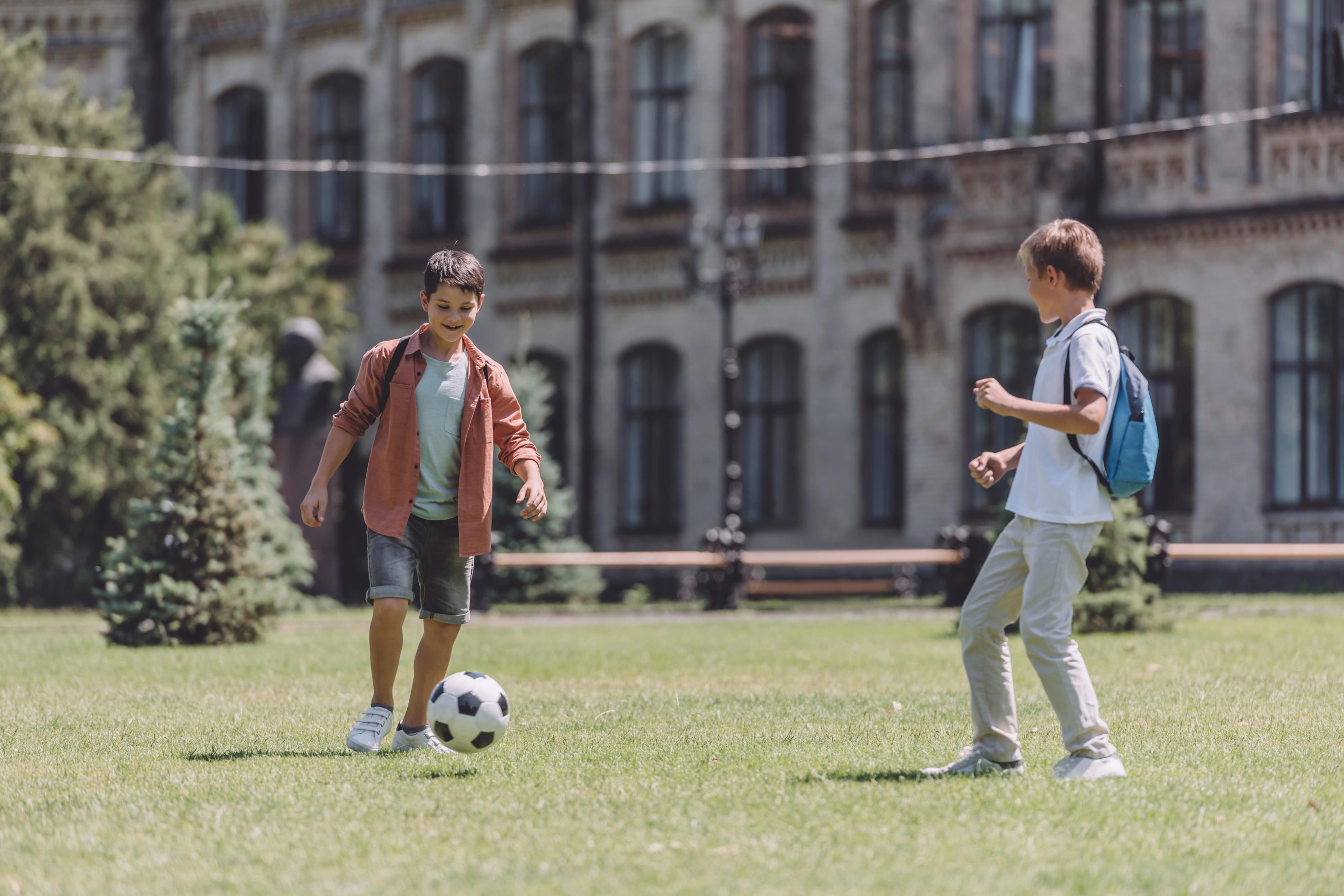 Kinder mit dem Ball vor einer Schule: Grünfläche statt Parkplatz