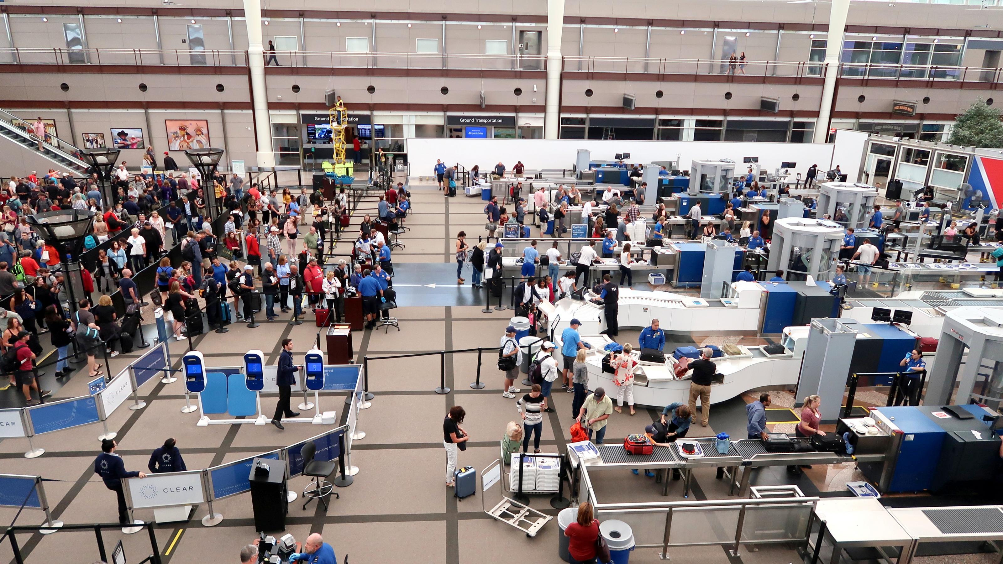 Eine lange Schlange von Menschen wartet vor den Metalldetektoren am Flughafen darauf, kontrolliert zu werden