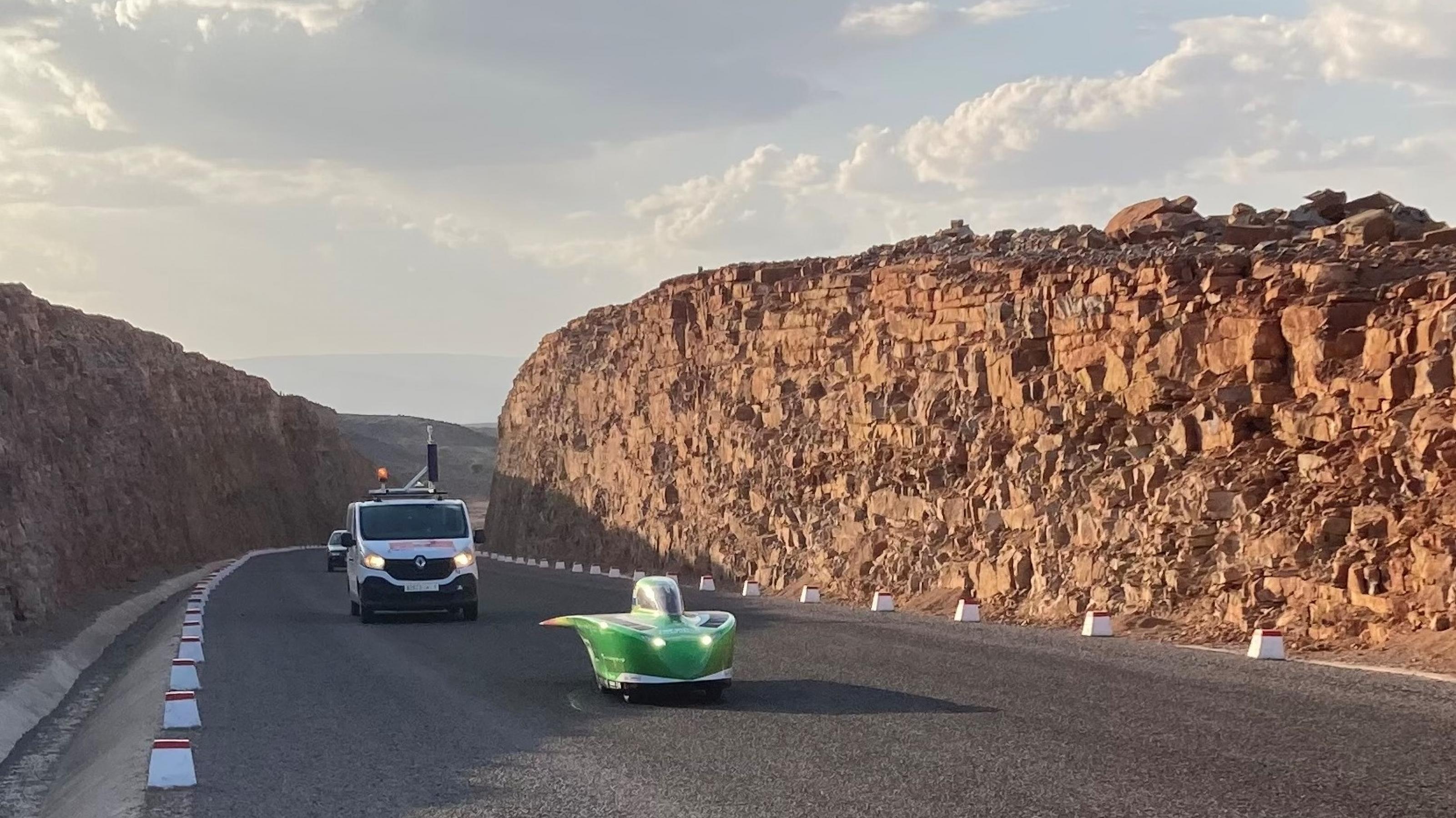 Ein mit Solarenergie betriebener Rennwagen fährt auf einer Passstraße durch das Atlasgebirge in Marokko, gefolgt von einem Teamfahrzeug.