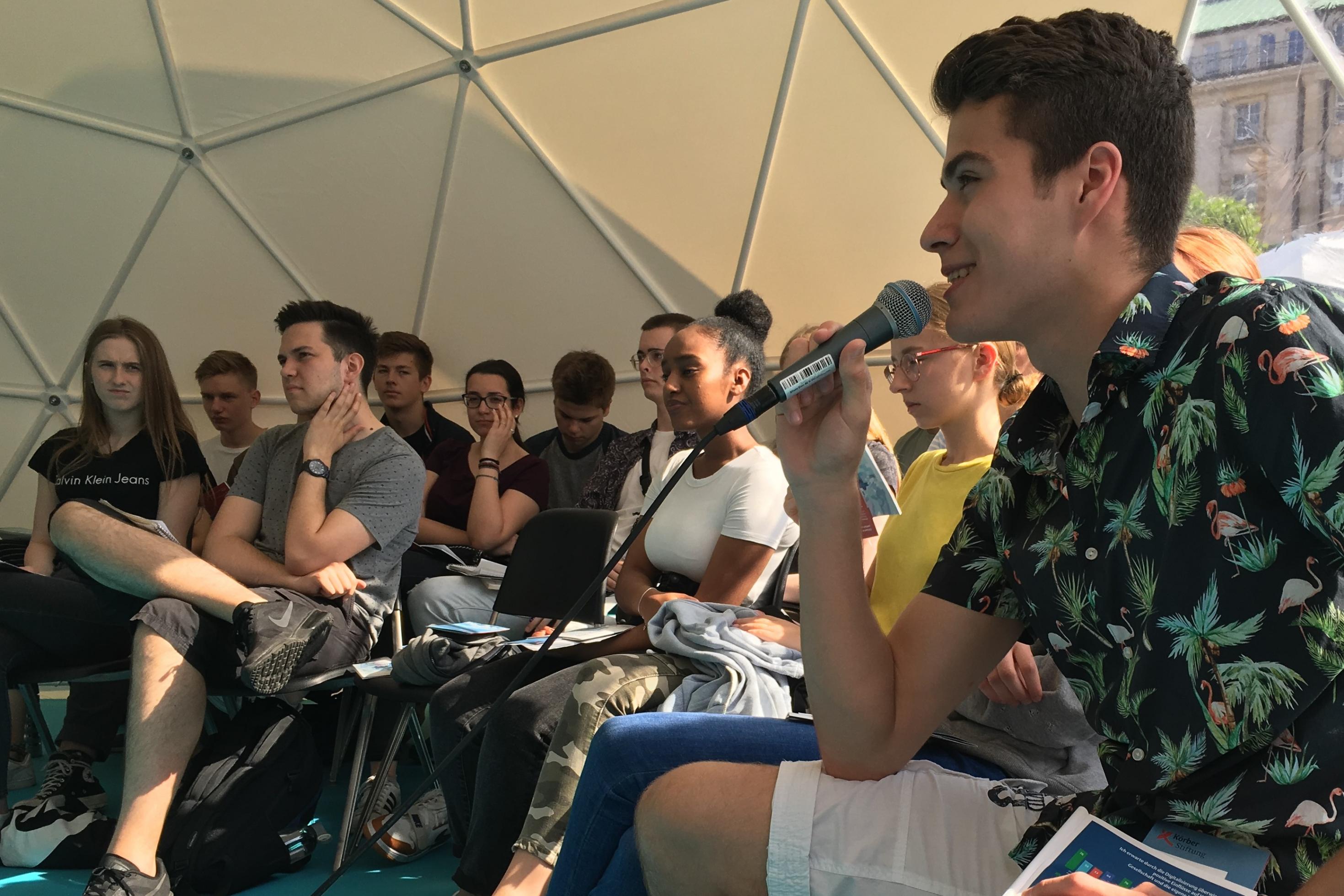 Beim Sommer des Wissens der Universität Hamburg sitzen Schüler in einem Zelt und diskutieren über Designerbabys. Die Zukunftsreporter moderieren.