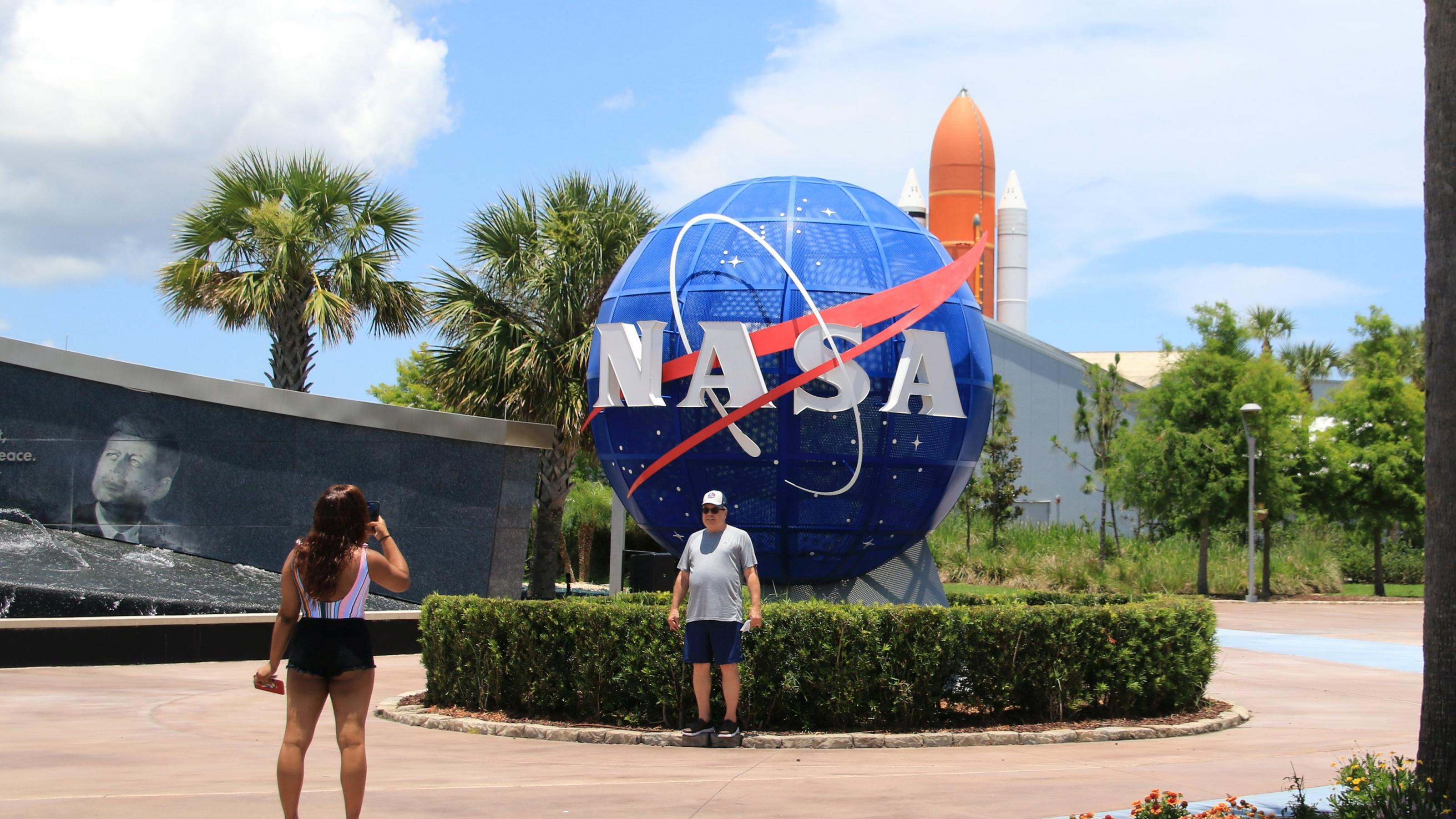 Eine Frau fotografiert einen Mann vor einem Logo der amerikanischen Weltraumbehörde NASA