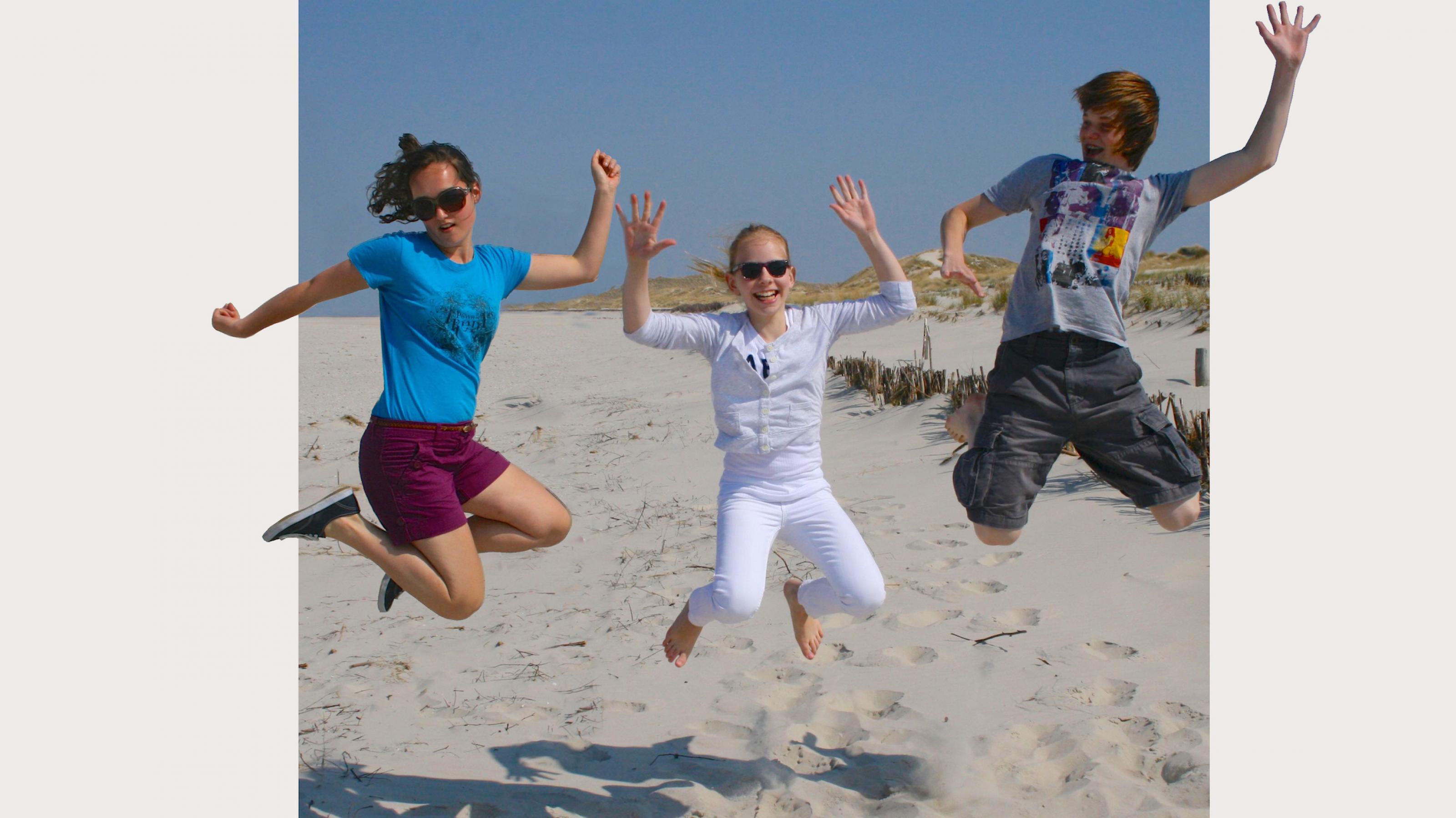 Drei Teenager springen am Strand in die Höhe; die Kamera friert ihre Bewegung im Flug ein. Ist das Lebensfreude, auch für die Eltern – oder doch nur eine Umweltbelastung?