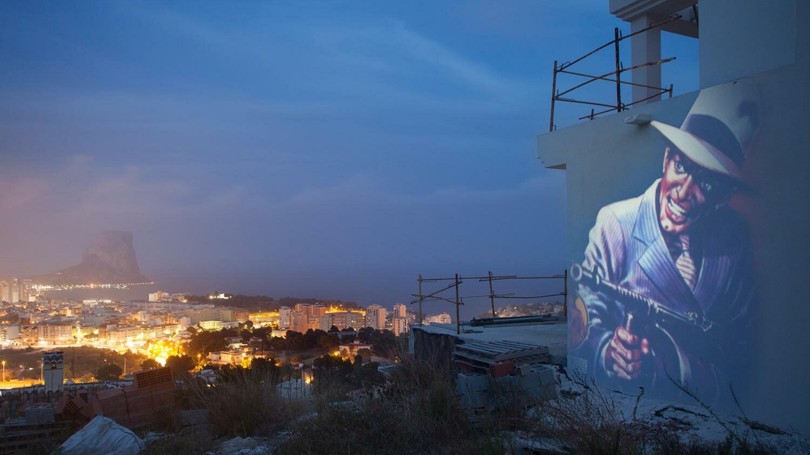 Projektion eines Gangsters auf der Wand einer Bauruine an der spanischen Küste. Im Hintergrund der Ort Calpe an der Costa Blanca