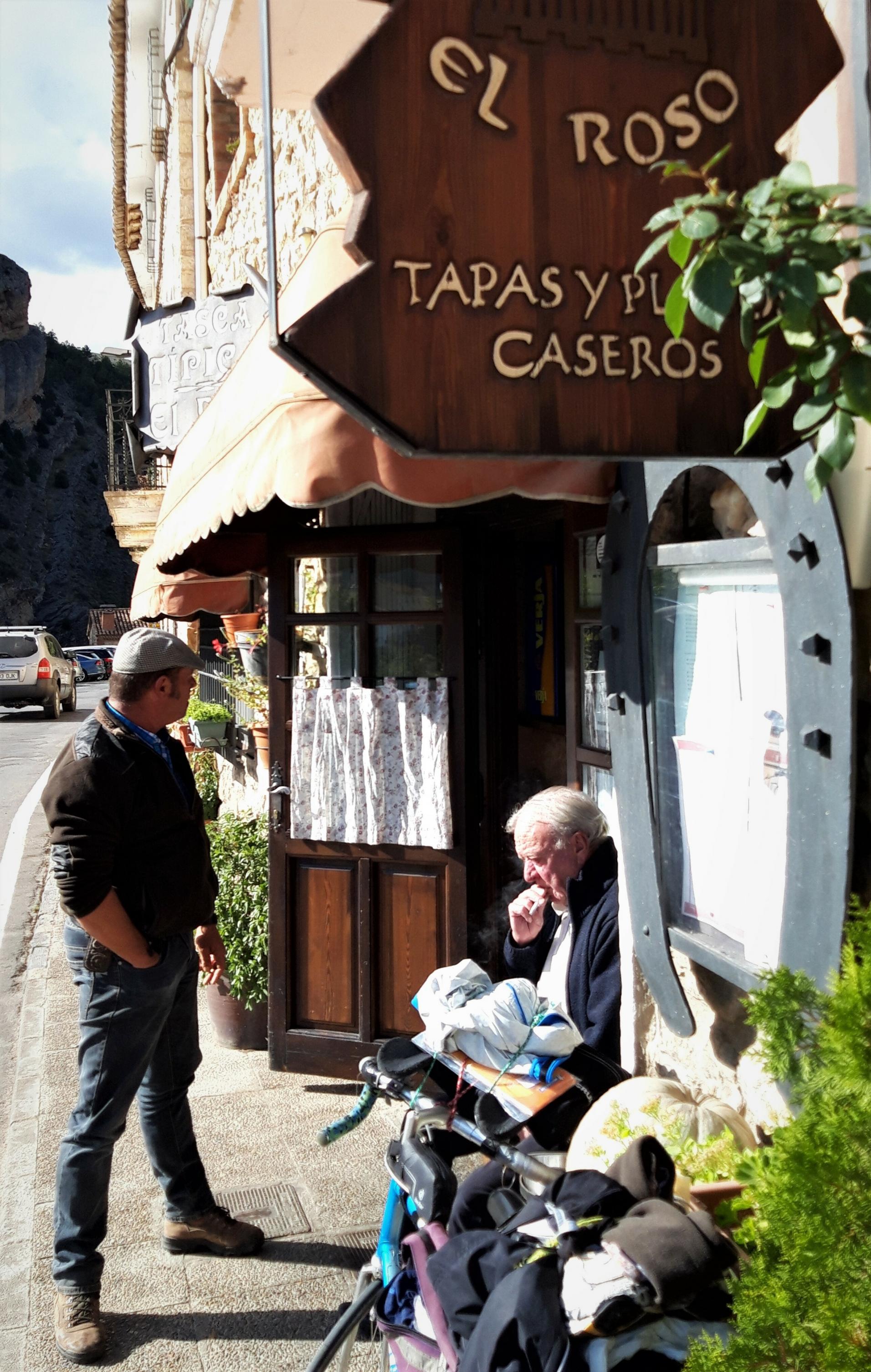 Zwei Männer vor der Taberna El Roso, einer stehend, der andere sitzend.