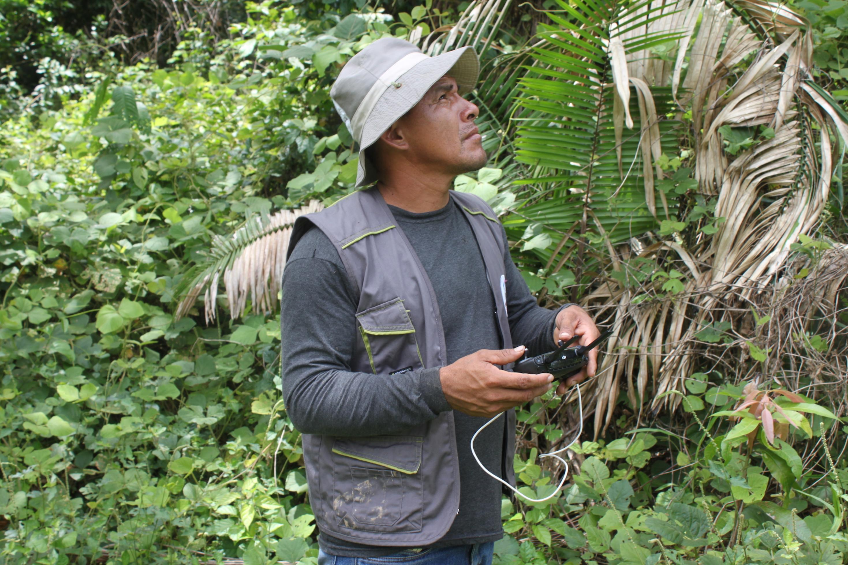 Ein indigen aussehender Mann steht im Regenwald und steuert eine Drohne.