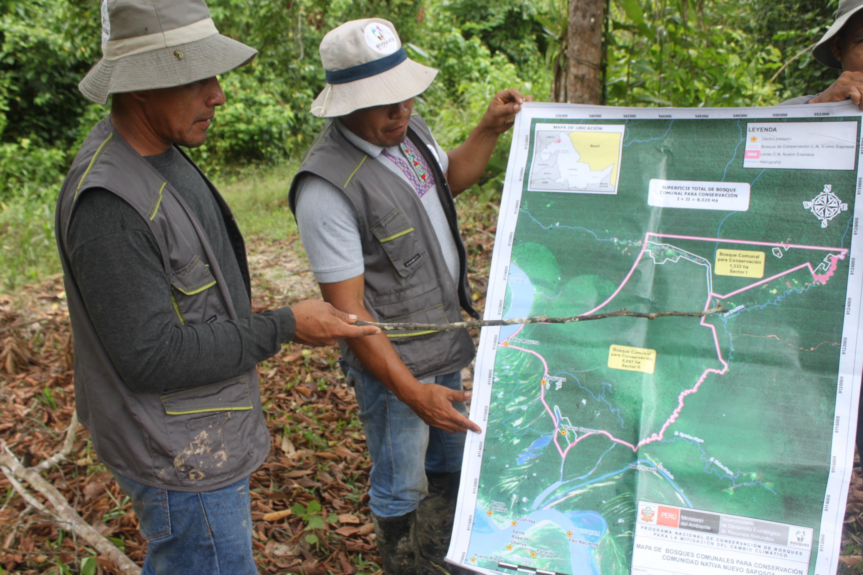 Zwei indigen aussehende Männer mit Trapperhut und Outdoor-Kleidung schauen auf eine grosse Landkarte ihres Gemeindegebietes.