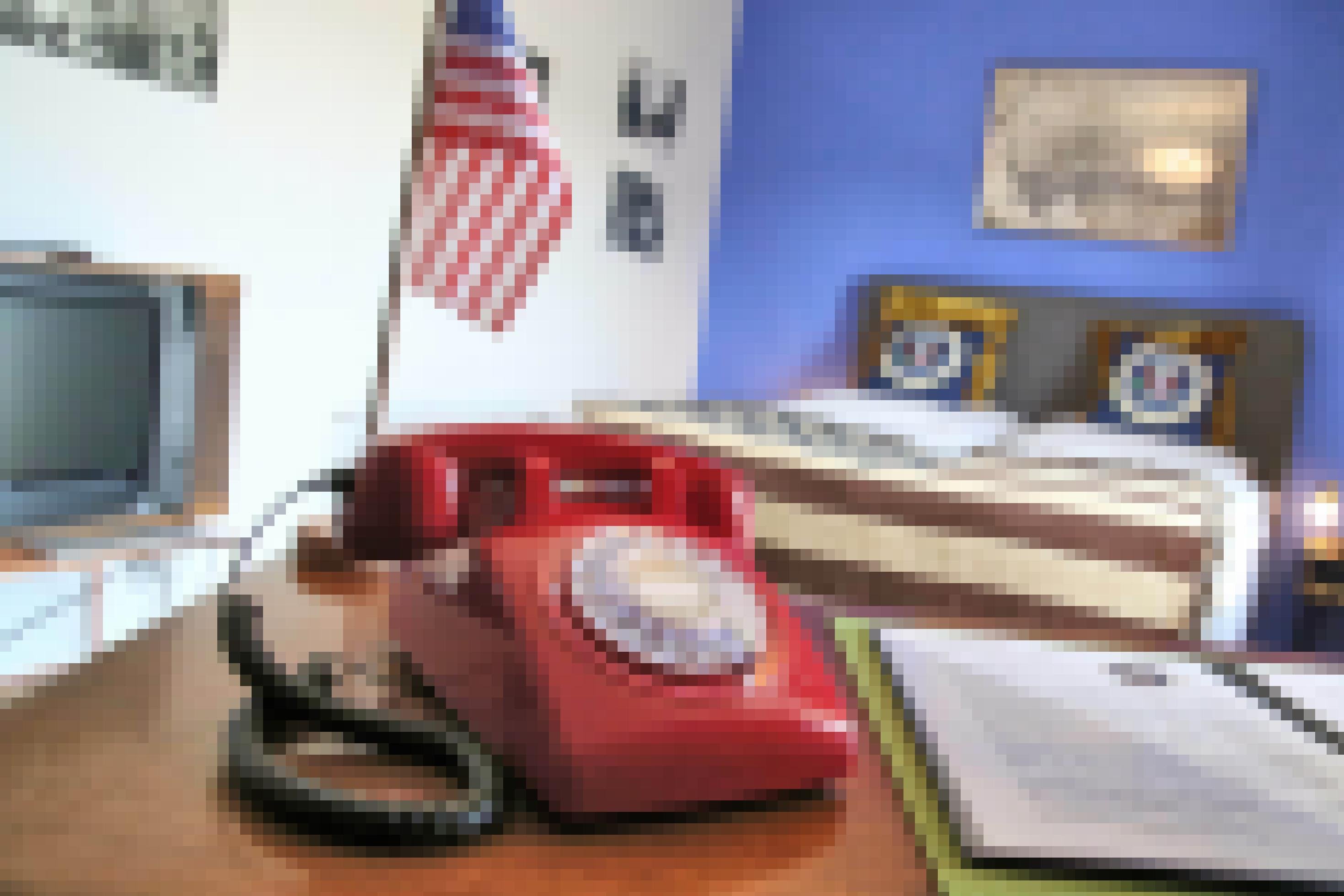 Ein rotes Telefon steht auf einem Schreibtisch. Im Hintergrund sind eine US-amerikanische Tischfahne sowie ein Doppelbett zu sehen.