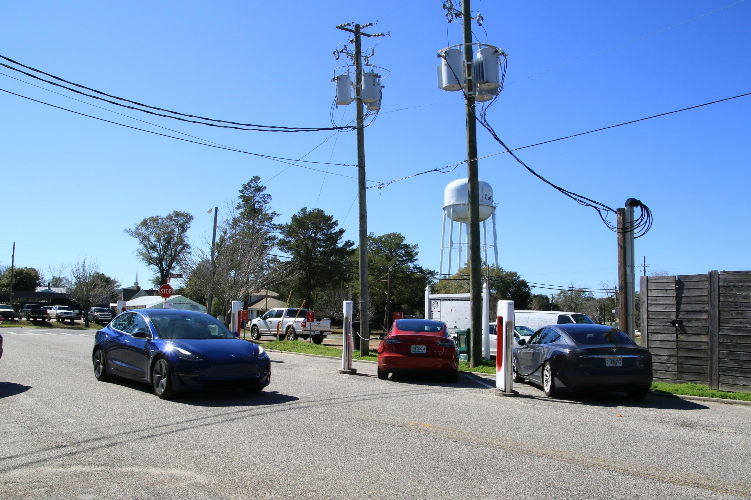 Ein Auto fährt über eine Straße, im Hintergrund parken zwei weitere Autos und zapfen Strom.