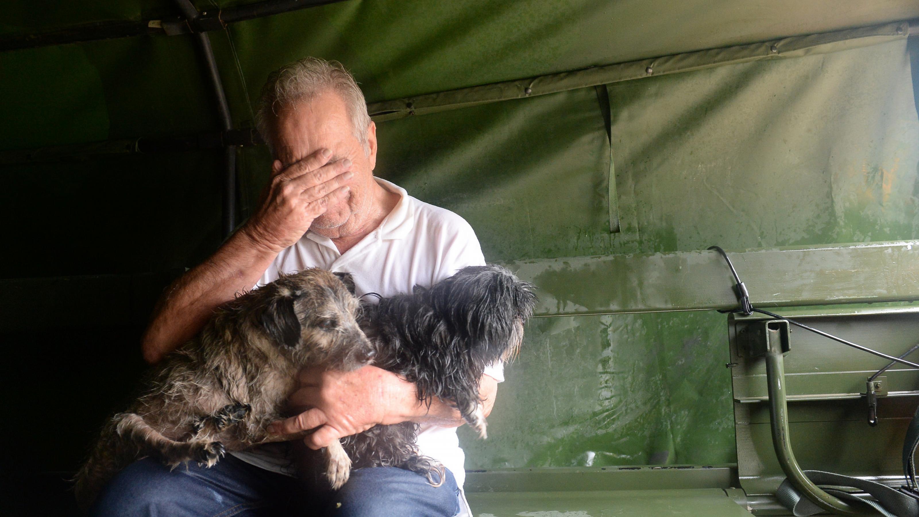 Ein älterer Mann sitzt auf einer Pritsche in einem Lastwagen. Er hat zwei kleine Hunde im Arm und hält sich die Hand vor die Augen. Er macht einen verzweifelten Eindruck. Seine Kleidung ist durchnässt. Die Texas National Guard war ihm zur Hilfe gekommen, als Hurrikan „Harvey“ im August 2017 sein Stadtviertel in Houston überschwemmte.