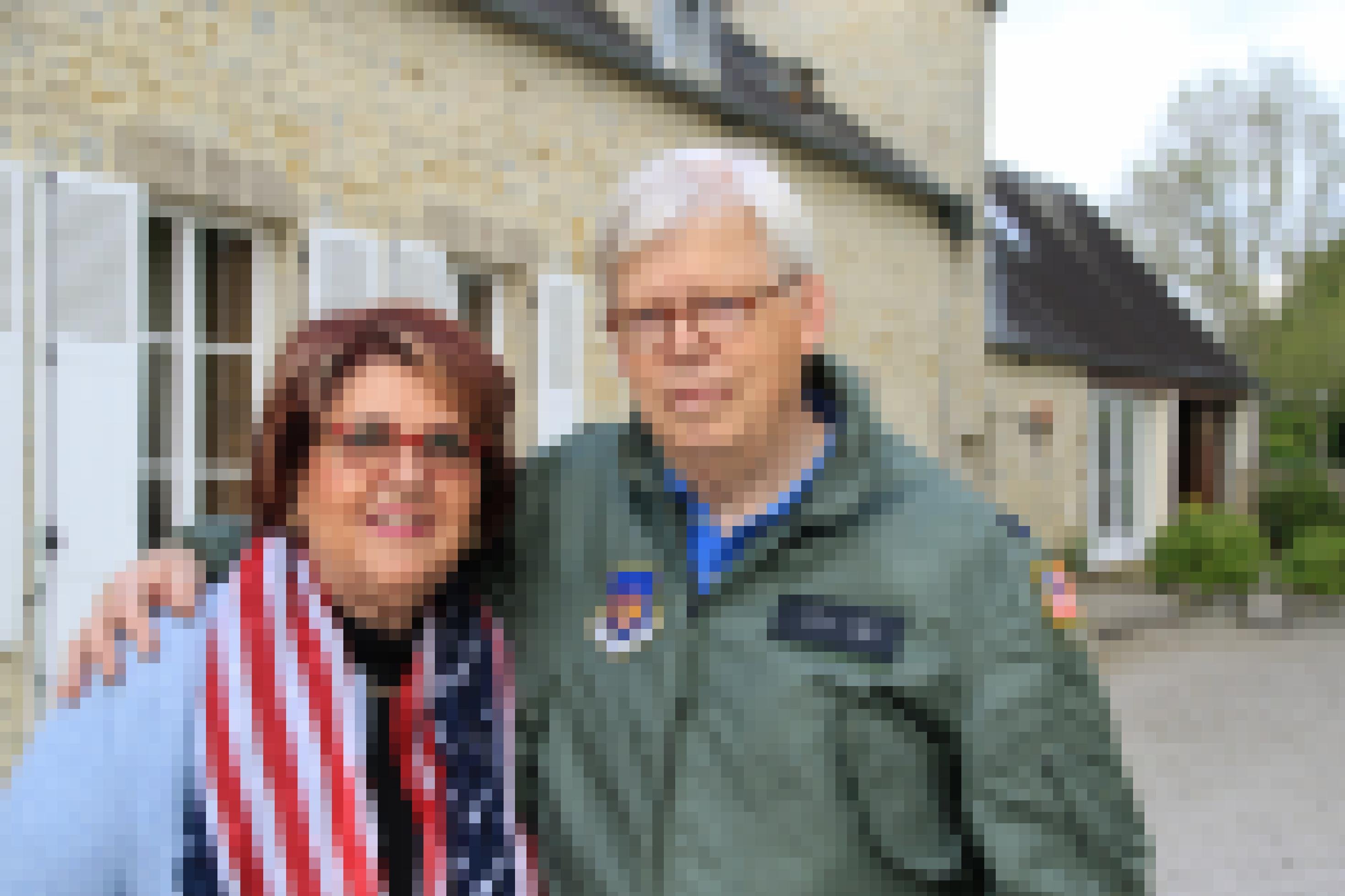 Ein älteres Ehepaar, er trägt Bomberjacke, sie einen Schal mit der US-Flagge