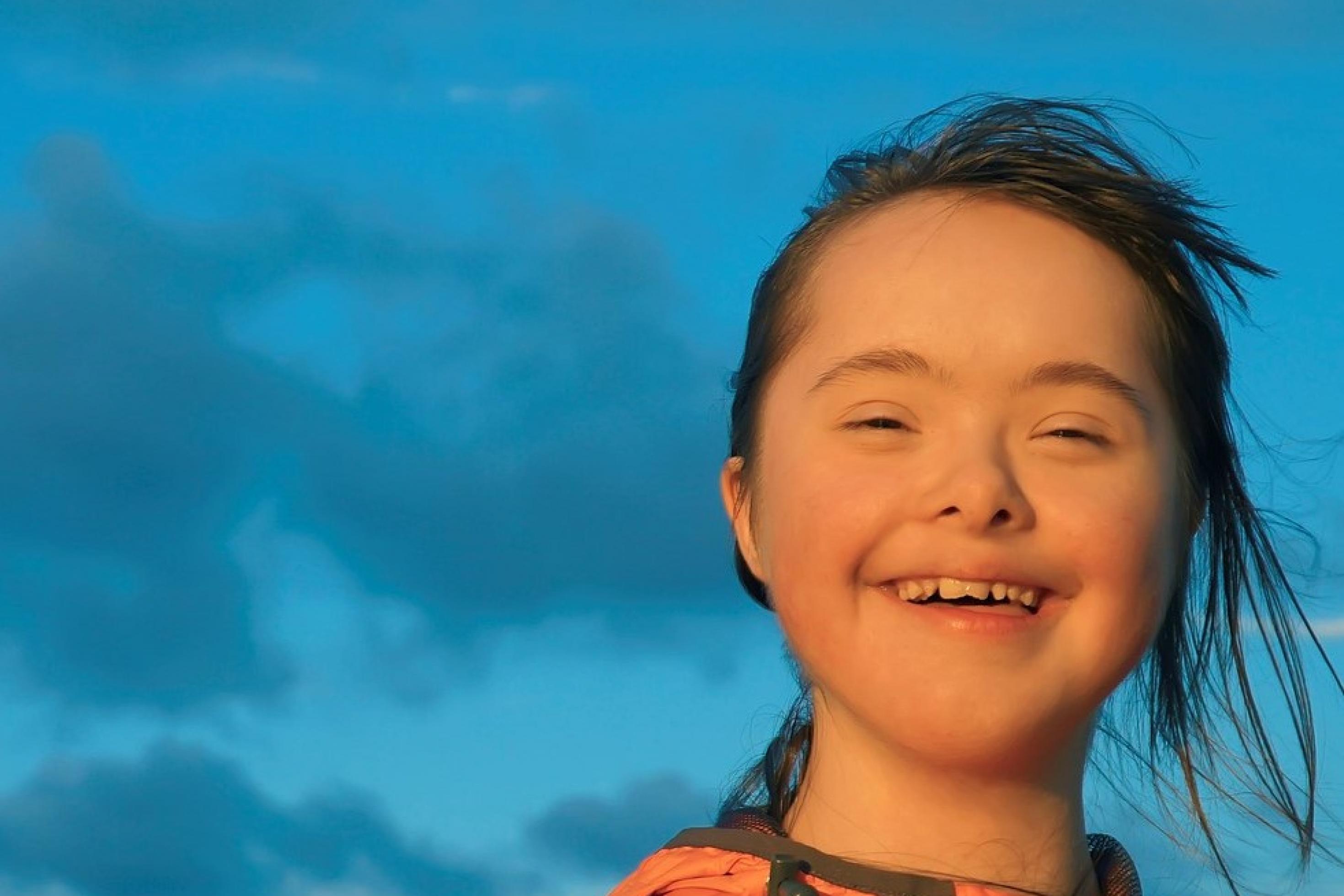 Lachendes Mädchen mit Down-Syndrom vor blauem Himmel