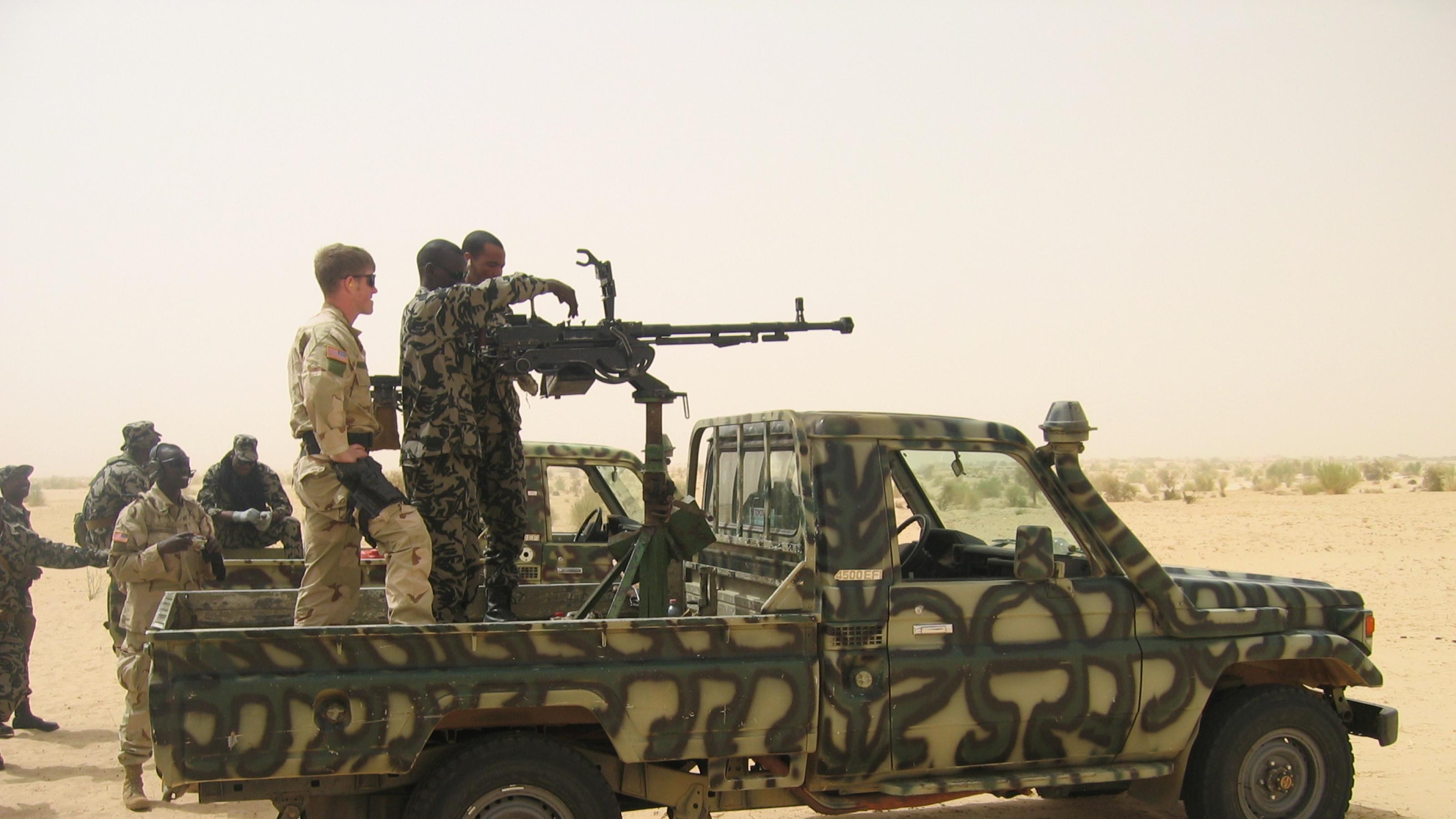 Zu sehen ist ein Pick-Up in militärgrün, in Tarnfarben. Auf der Ladefläche ist ein Geschütz aufmontiert, die Luft ist von Sand verhangen. Am Geschütz stehen US-amerikanische und malische Soldaten – offensichtlich eine Trainingssituation.