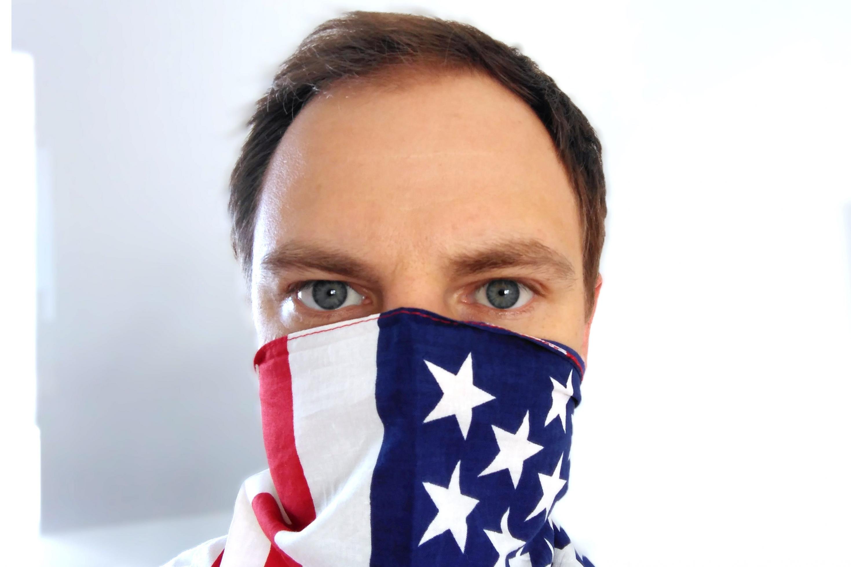 Nahaufnahme eines Gesichts, dessen Mund und Nase mit einer USA-Fahne bedeckt sind.