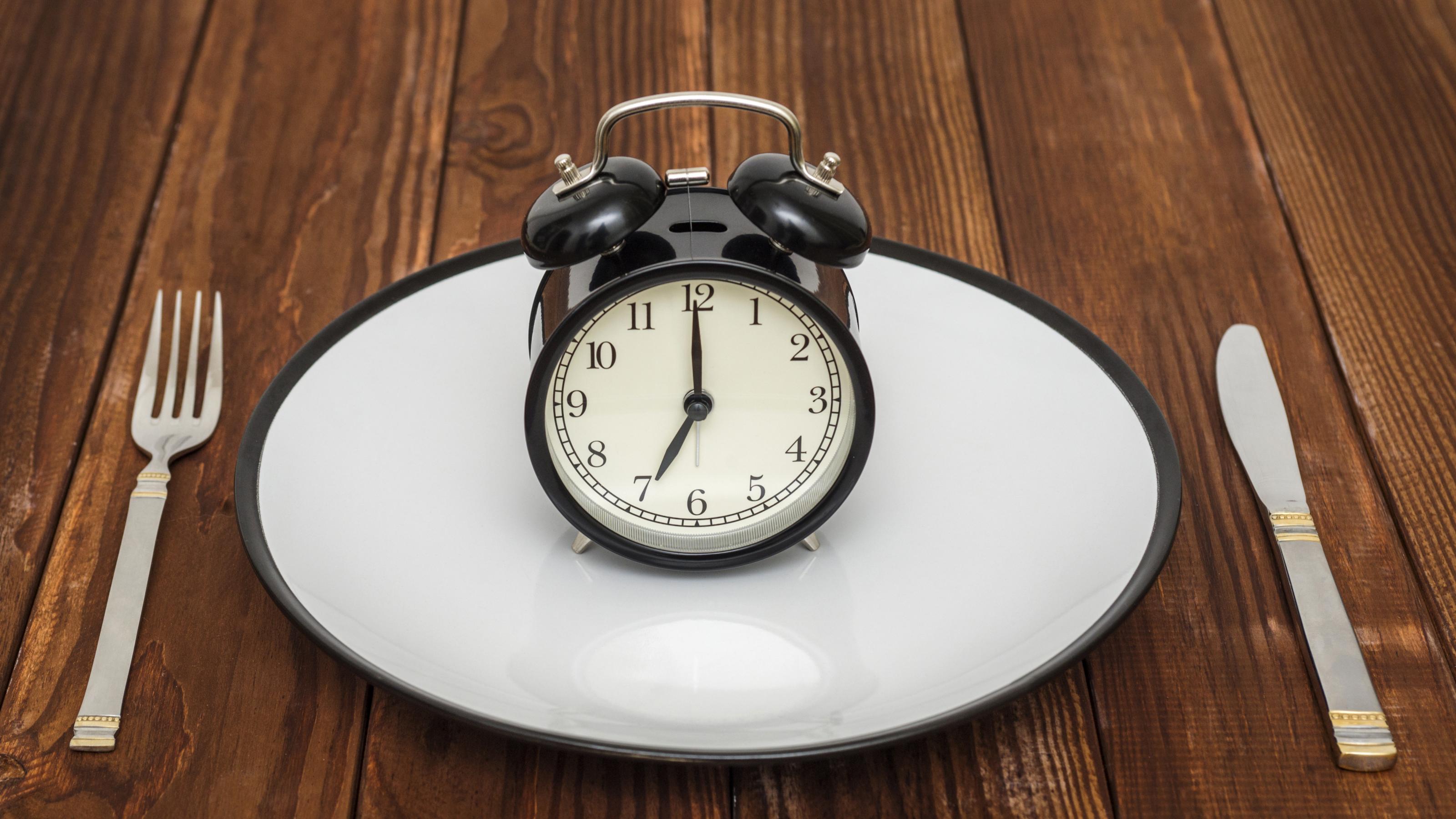 Alarm clock on plate with knife and fork on wooden background. Weight loss or diet concept