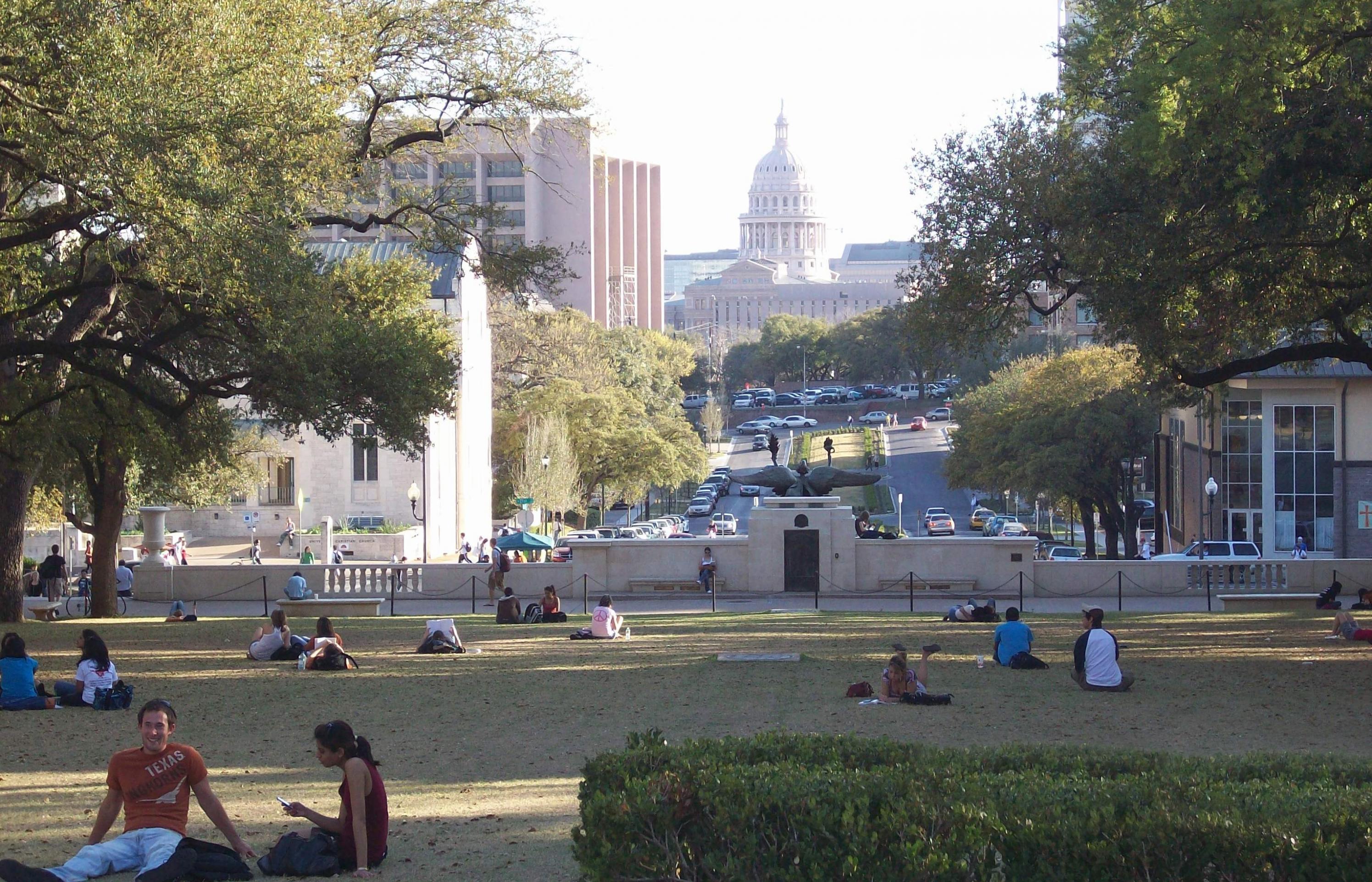 Junge Leute sitzen auf einer Wiese. Im Hintergrund ist das Capitol von Austin, Texas zu sehen.