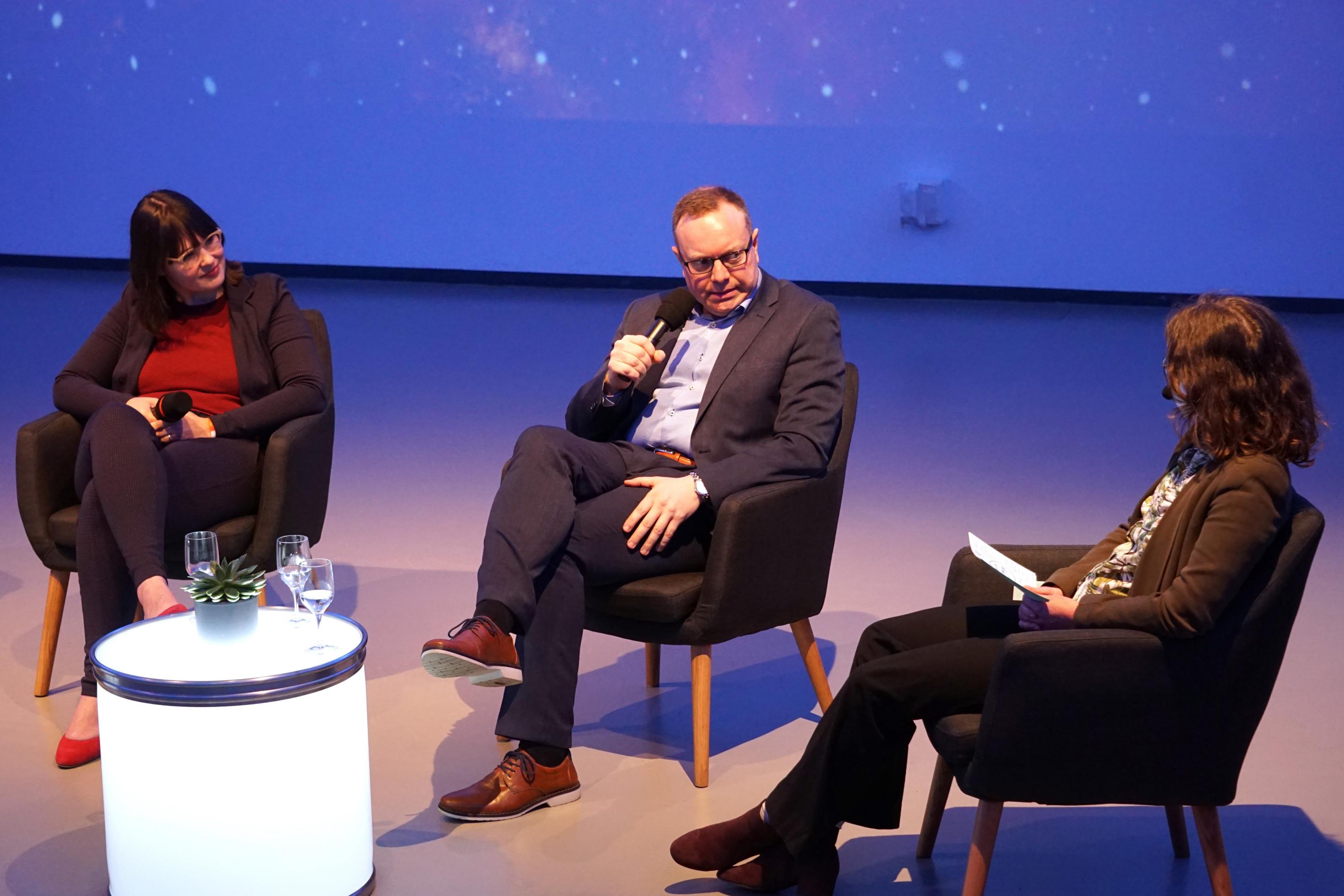 Drei Personen im Sitzen bei einer Podiumsdiskussion