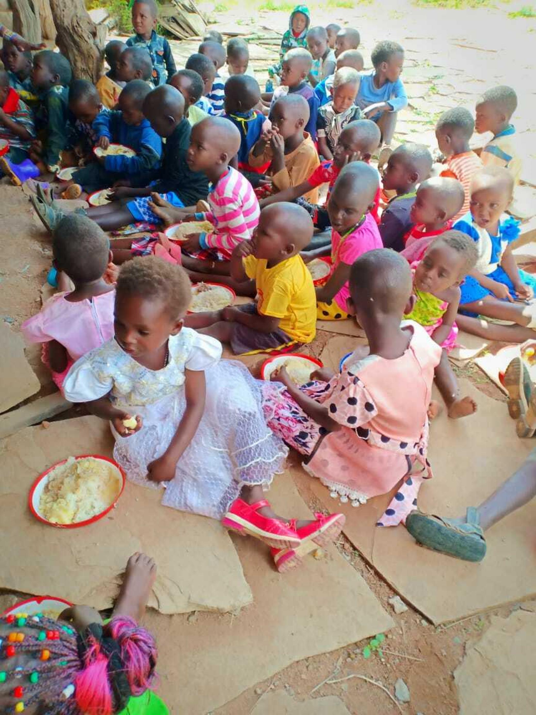 Massai-Kinder sitzen auf dem Boden, sie werden von Ellie Modesta unterrichtet.