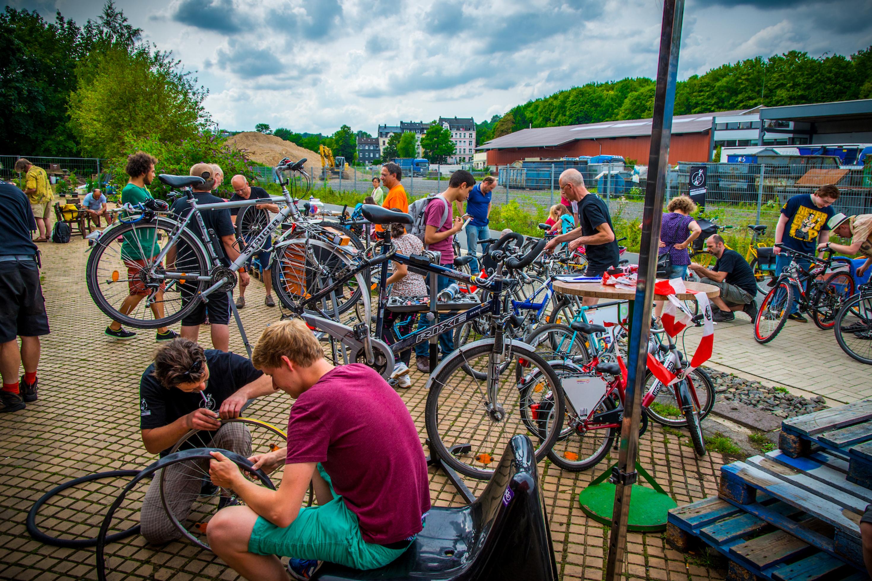 Viele Menschen auf einem Hof, die Fahrräder reparieren und sich dabei unterstützen.