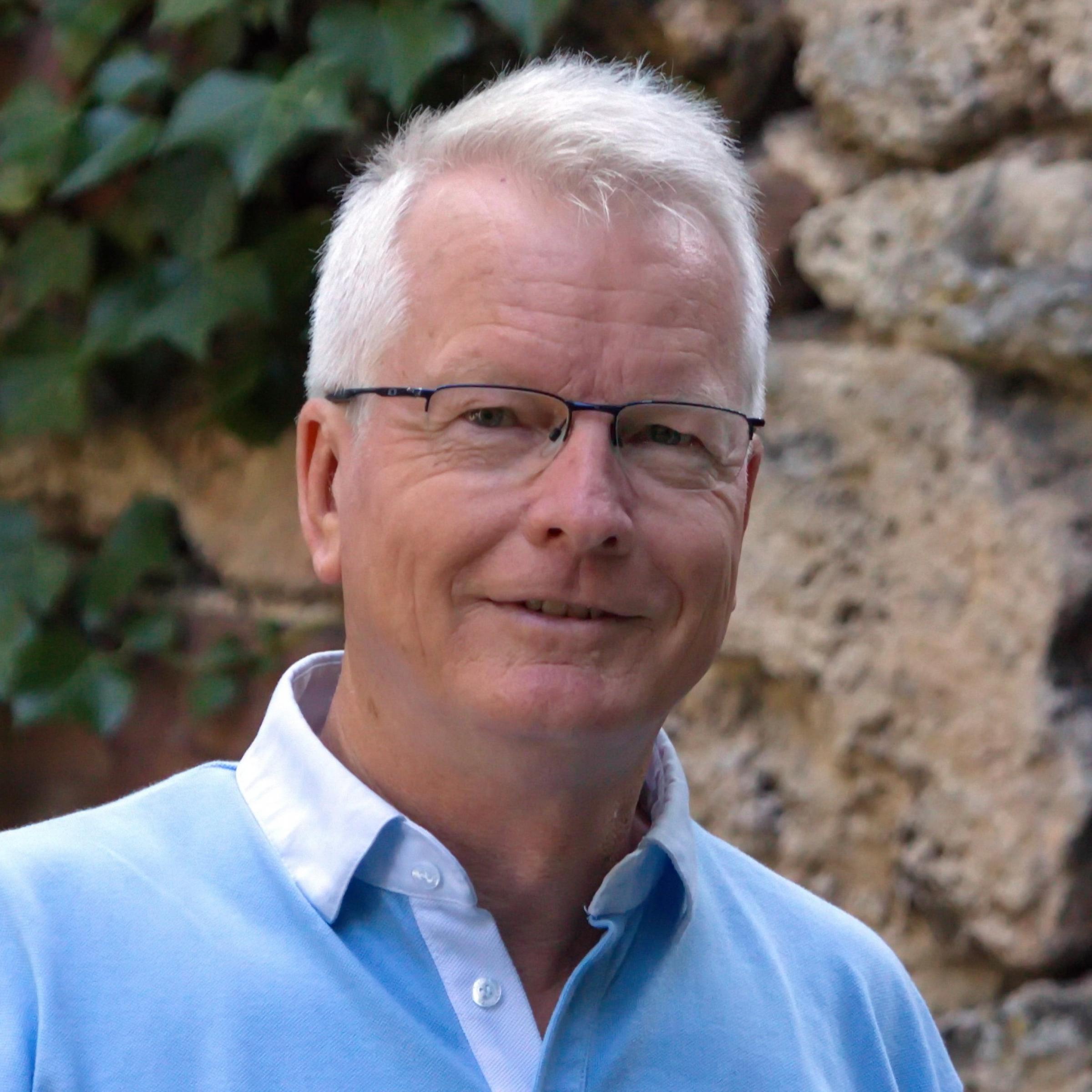 Porträt eines lächelnden Mannes mit Brille und kurzen, hellen Haaren