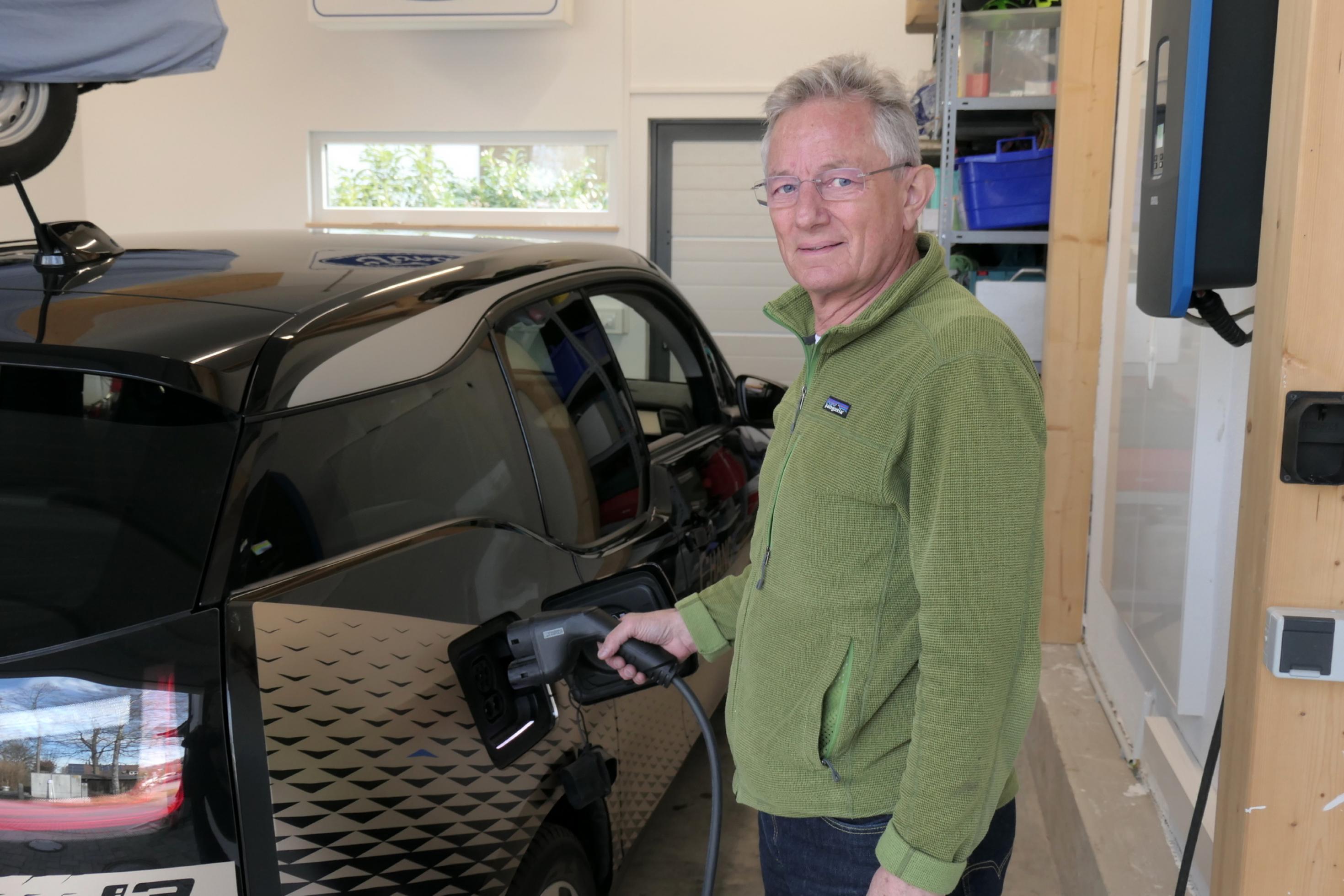 Xaver Pfab in seiner Garage neben einem BMW i3, der durch einen Ladestecker mit der Wallbox an der Wand verbunden ist.