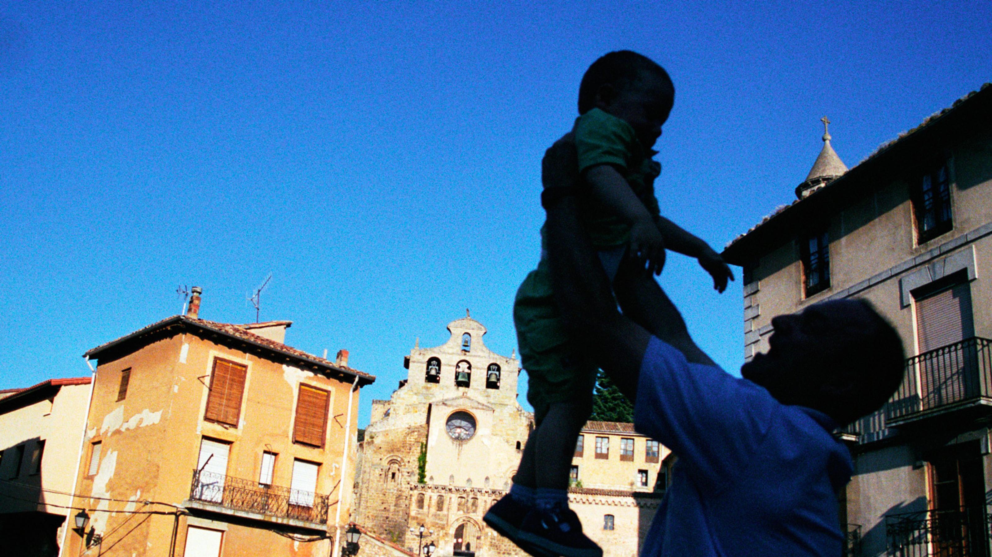 Ein Vater erfreut sich an seinem Sohn, wirft ihn in die Höhe auf dem Marktplatz eines Dorfes in Spanien.