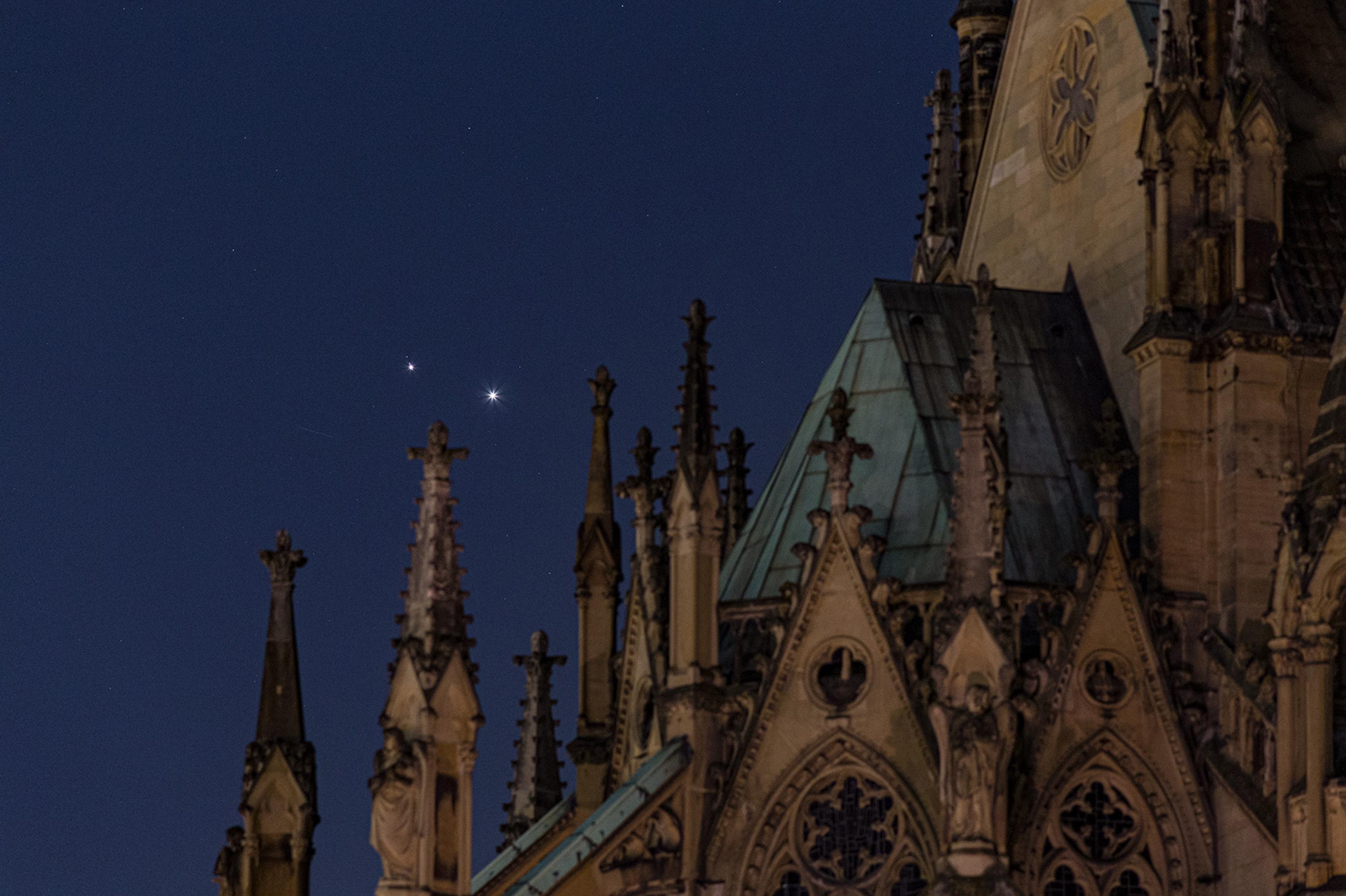 Am Himmel über einem Kirchendach sind zwei helle, eng beieinander stehende Lichtpunkt zu sehen.