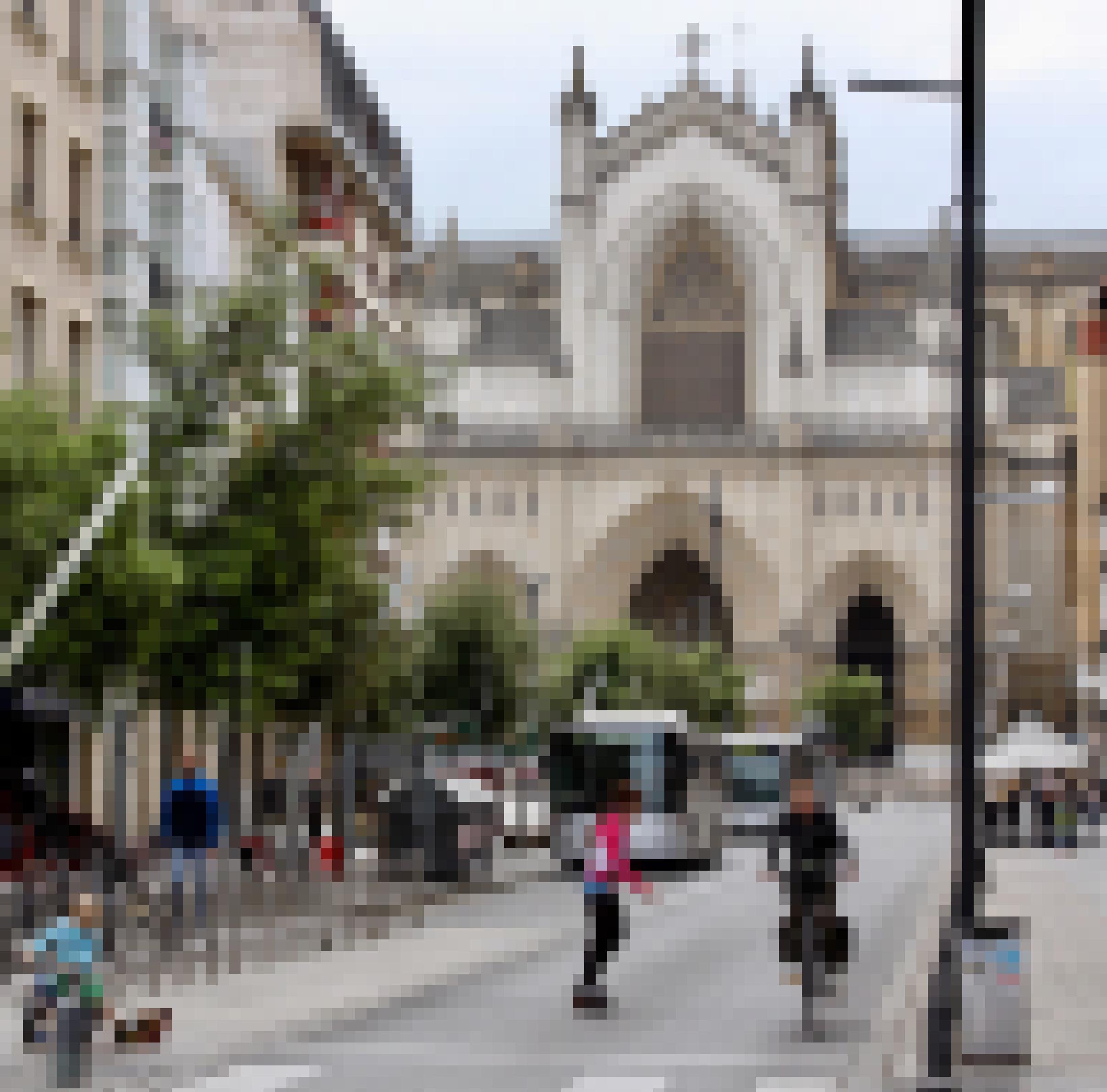 Blick auf eine Bushaltestelle mitten in der Stadt. Im Hintergrund ist eine Kathedrale zu sehen. Im Vordergrund ein Radfahrer und eine Skaterin.