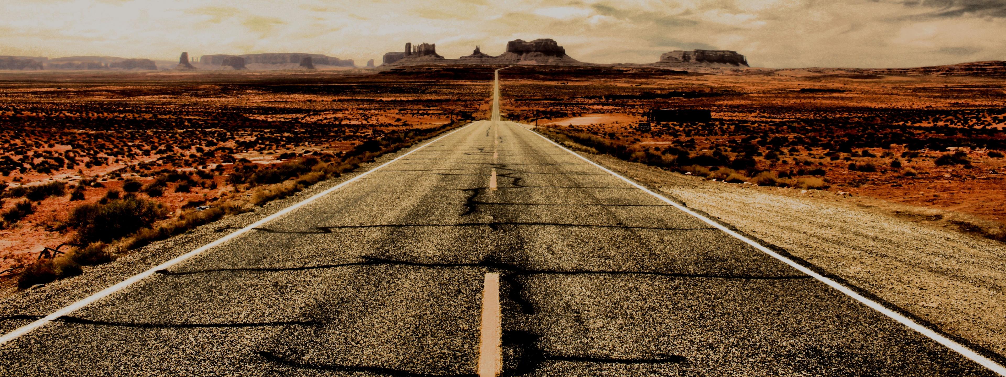 Eine Straße in der Wüste, die zu einer weit entfernten Felsformation führt.